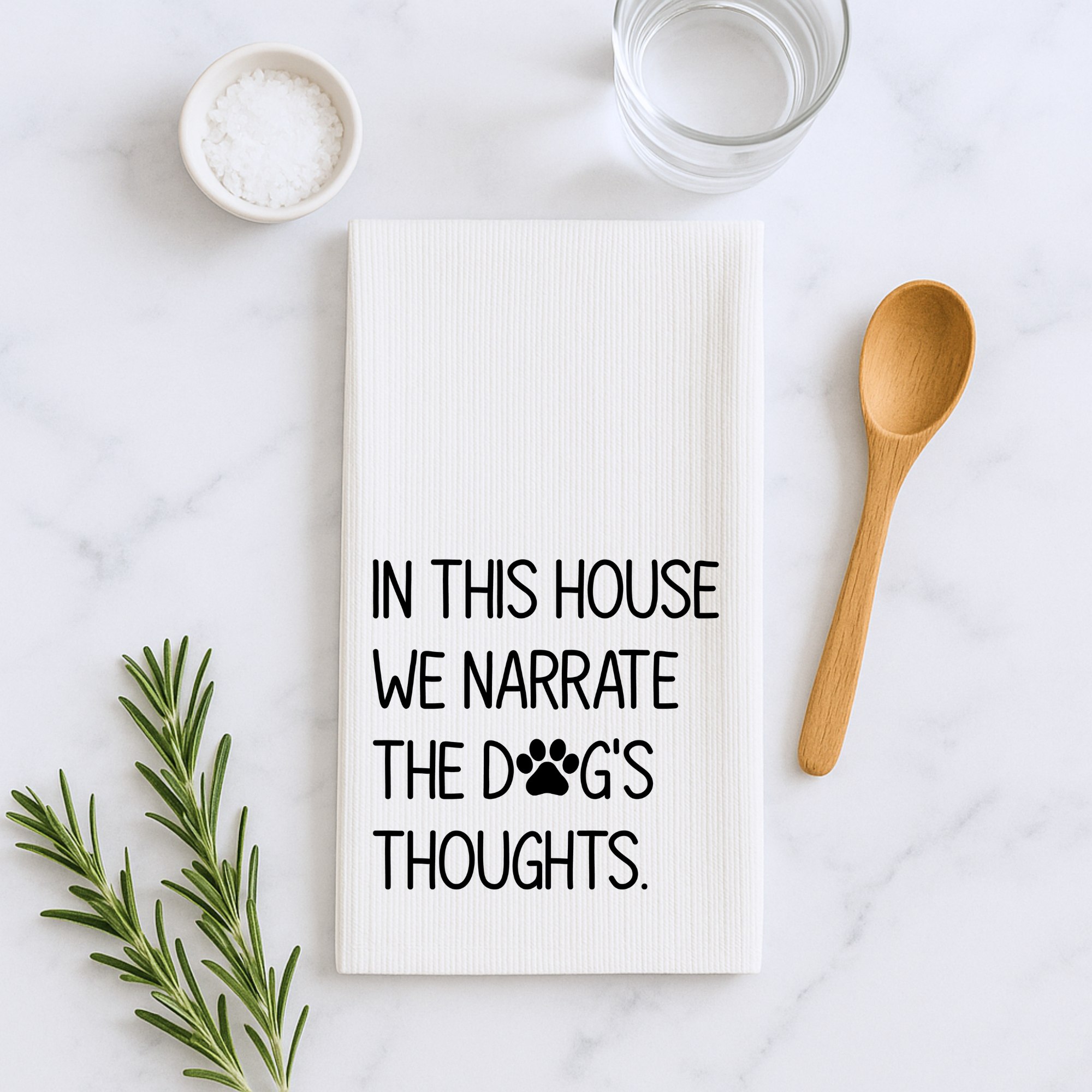 Premium kitchen towel with black dog lover quote design on a marble countertop with rosemary and wooden spoon.