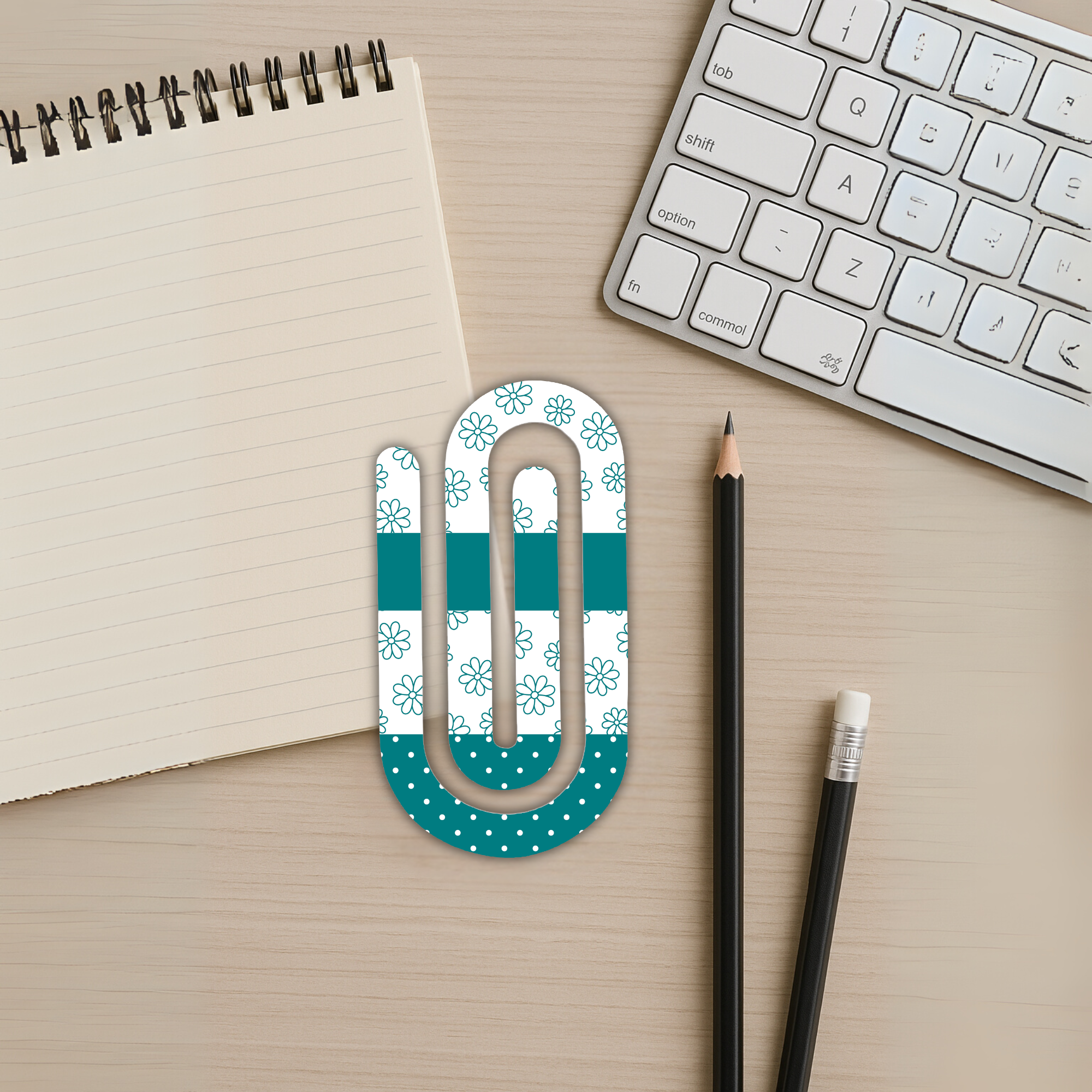 Jumbo acrylic paperclip with floral and polka dot design on a notebook and keyboard desk setup.
