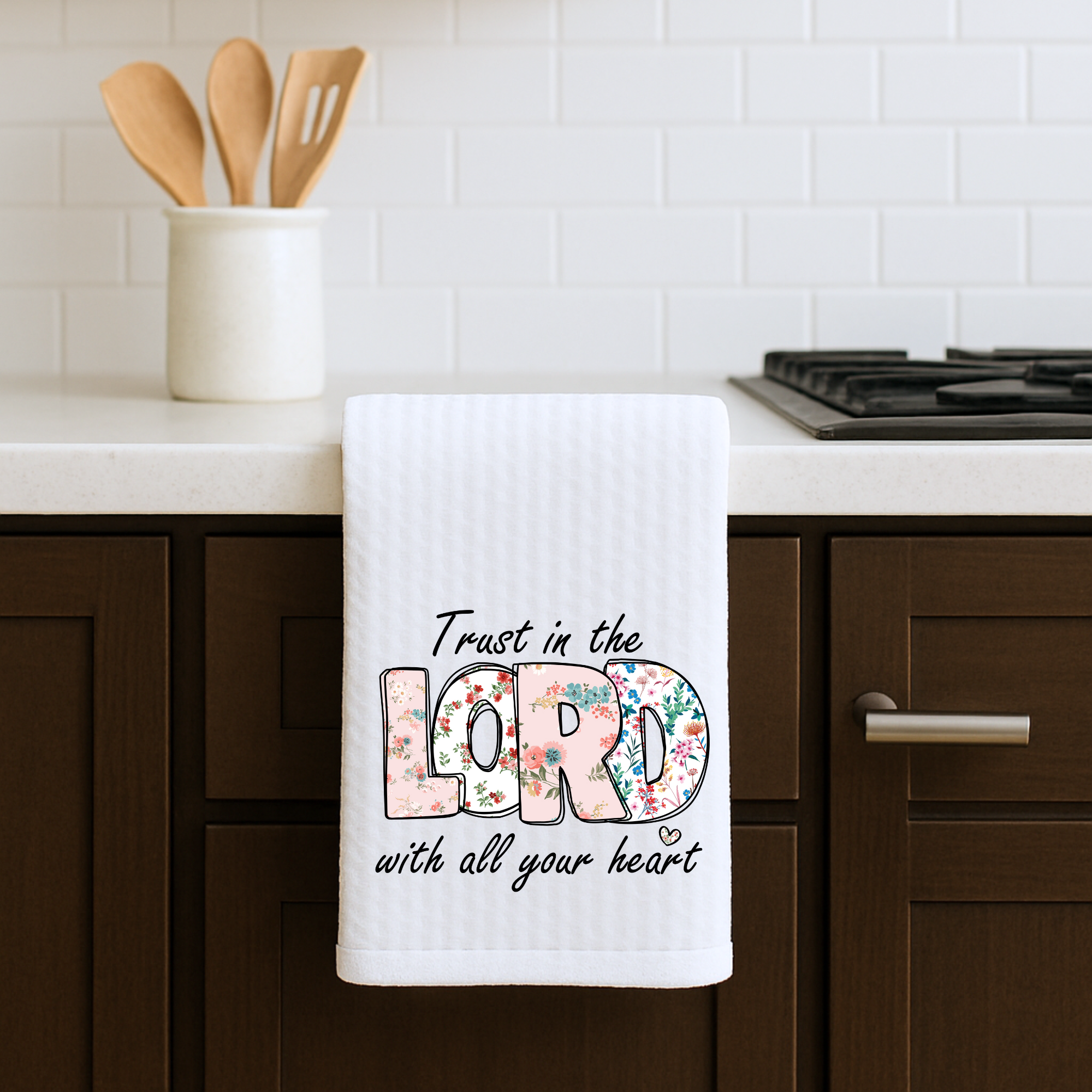 Bible verse kitchen towel with Trust in the Lord floral text on stove cabinet.
