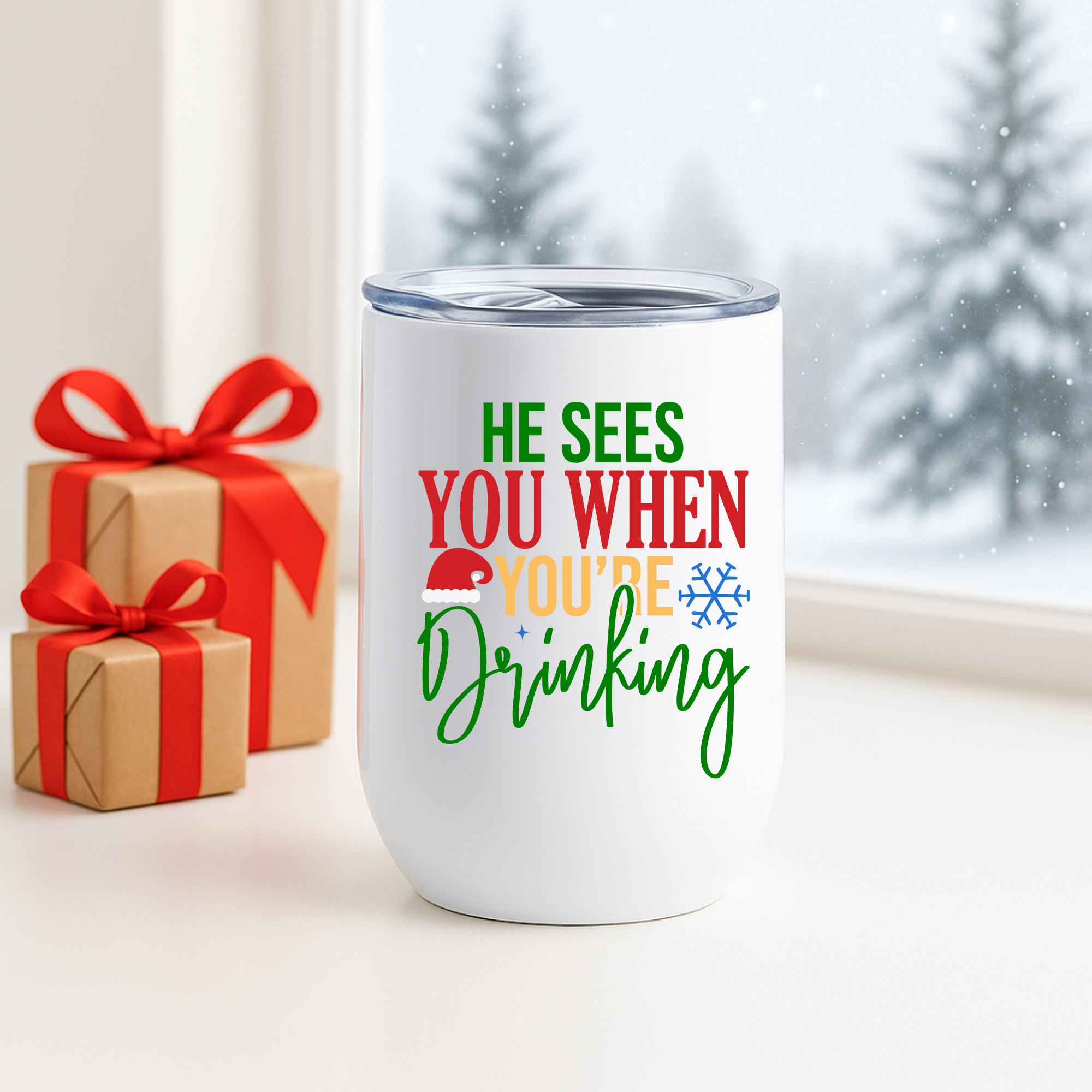 Christmas tumbler with funny “He Sees You When You’re Drinking” quote shown near wrapped gifts and snowy window backdrop.