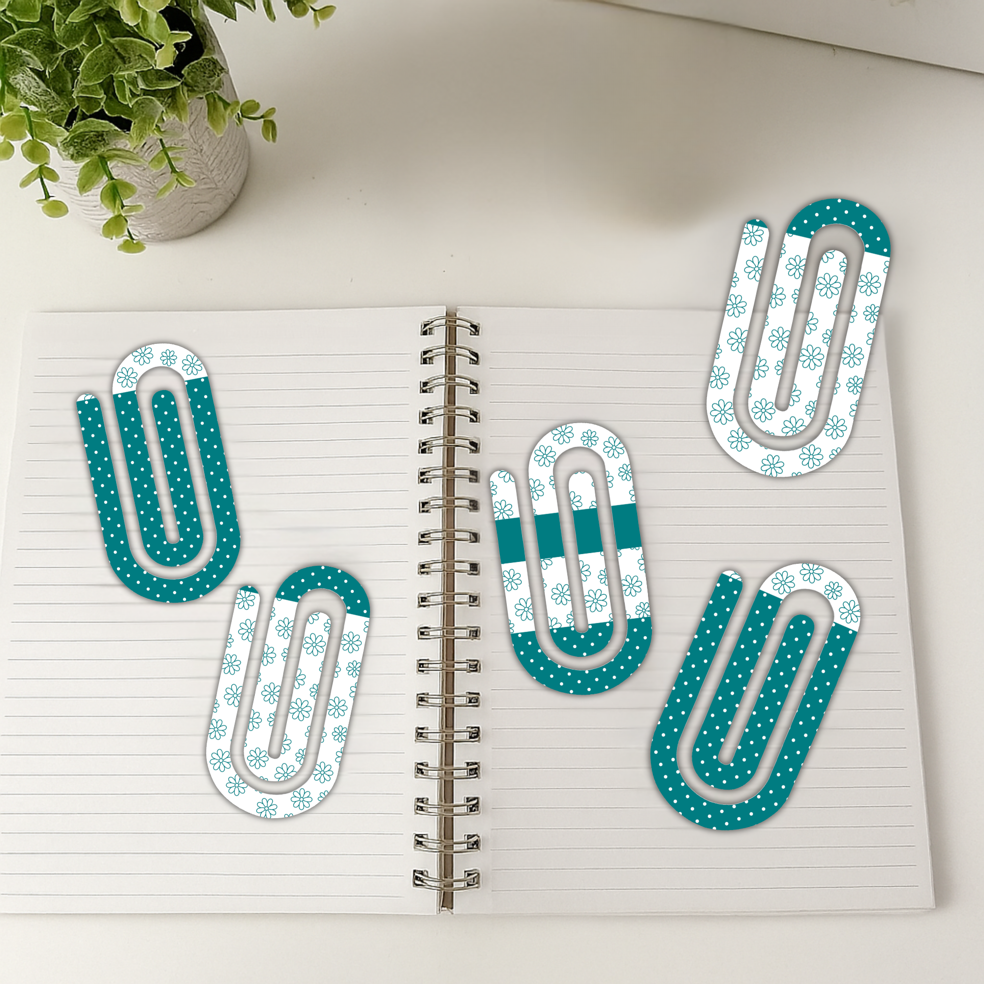 Multiple jumbo paperclips with floral patterns arranged on an open lined notebook.