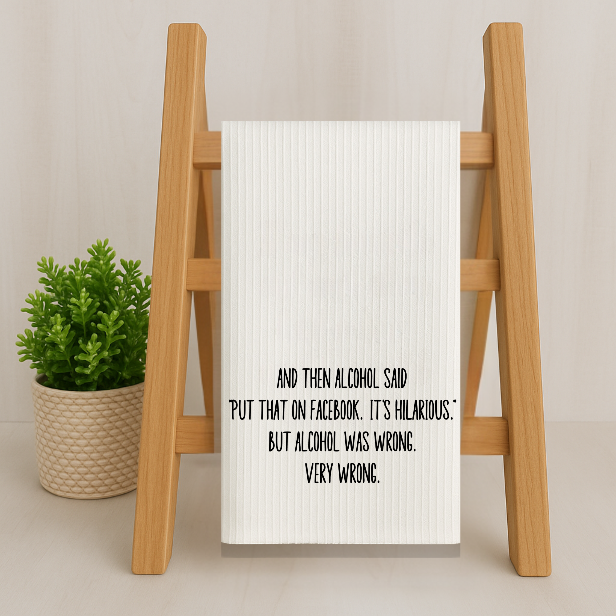 Funny microfiber kitchen towel with sarcastic alcohol quote, hanging on a wooden ladder with potted plant decor.