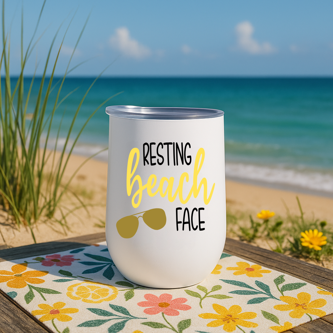 White wine tumbler on floral mat by beach with “Resting Beach Face” design in yellow and sunglasses graphic.