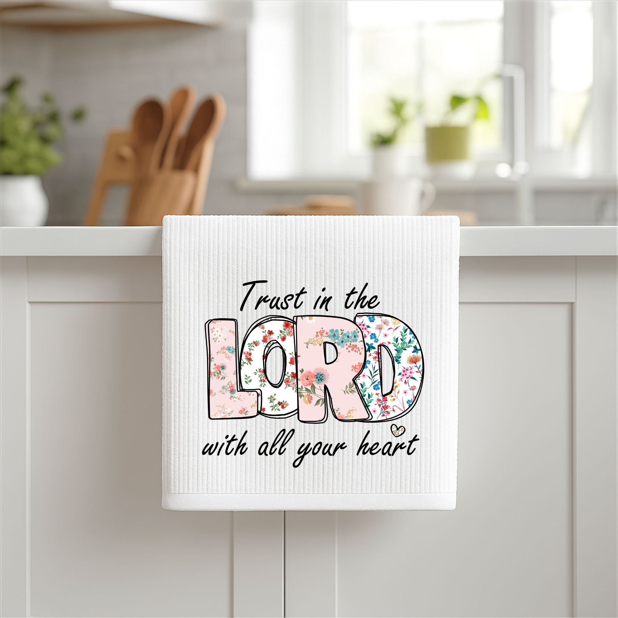 Christian floral kitchen towel with Trust in the Lord Bible verse hanging on cabinet.