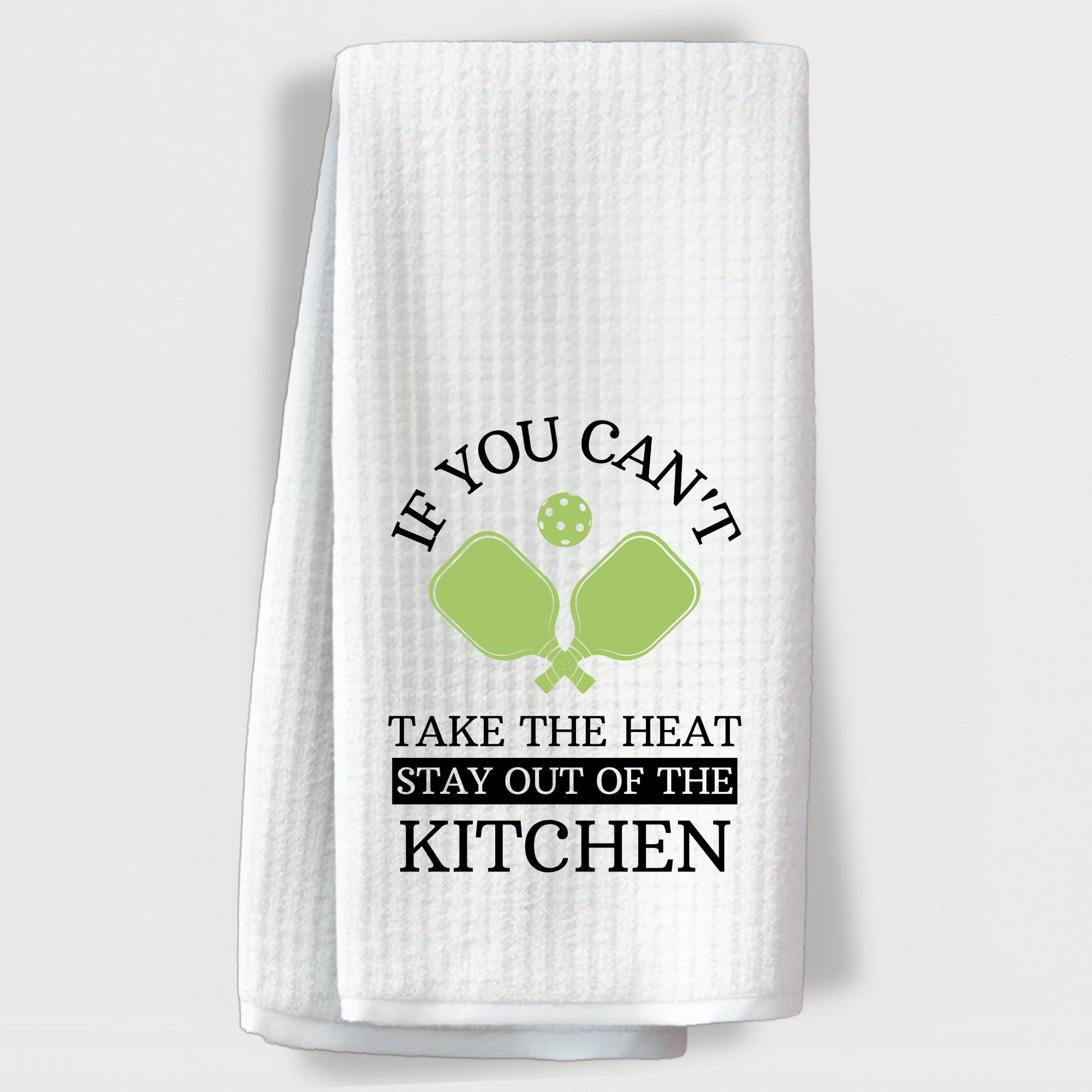 "Pickleball-themed towel with crossed paddles and the saying 'If you can’t take the heat, stay out of the kitchen'."