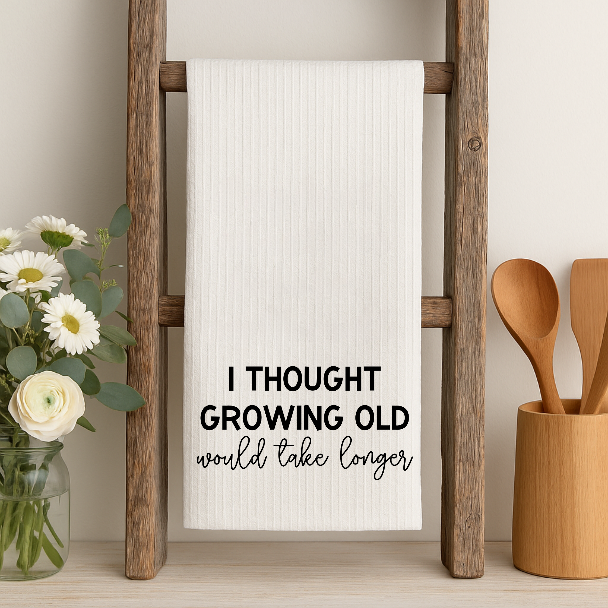 Farmhouse kitchen towel with growing old humor quote on rustic ladder with utensils.
