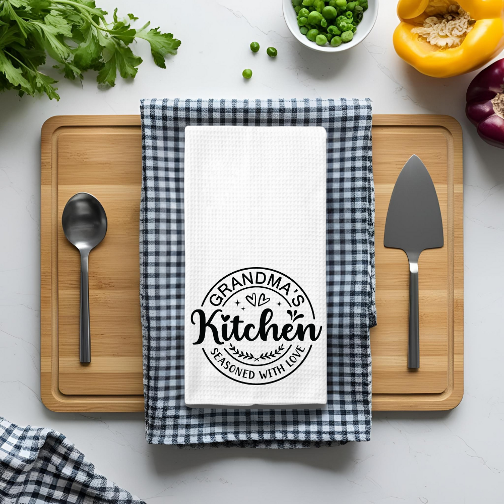 Funny kitchen towel for grandma, featuring a heartfelt quote, folded on a checkered cloth with fresh vegetables and kitchen tools.