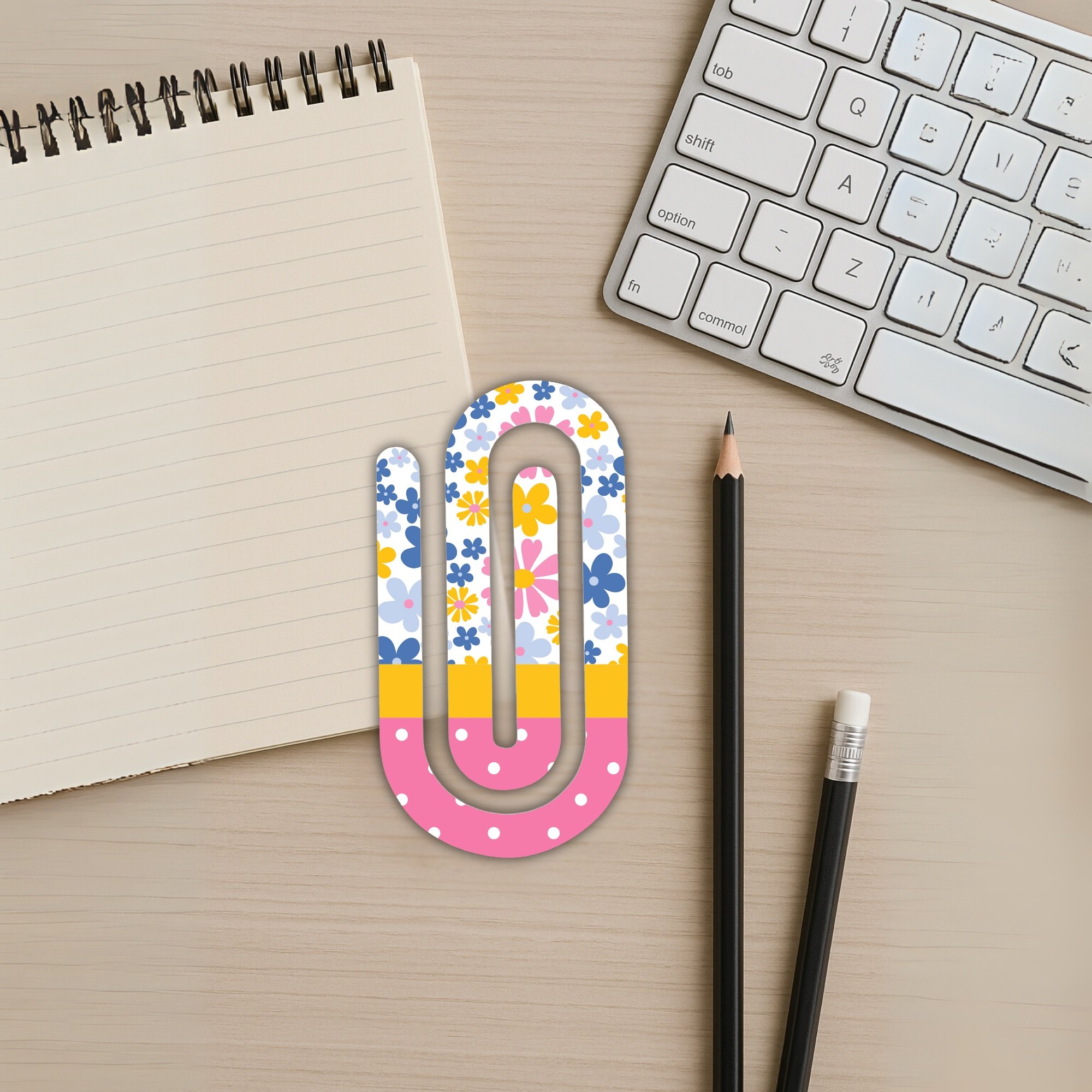 Floral jumbo paper clip on desk next to spiral notebook and keyboard.