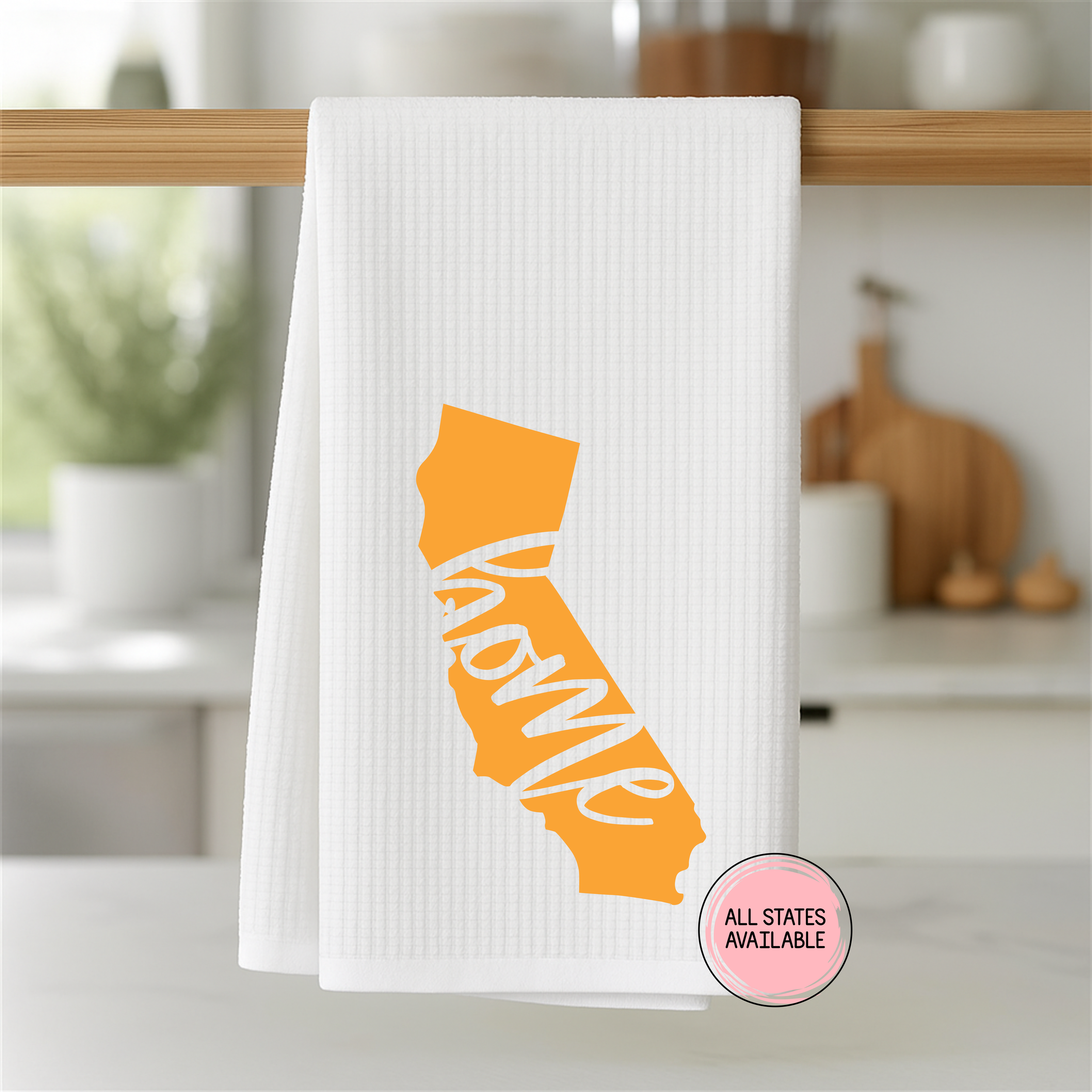California home state kitchen towel in orange on a white waffle weave towel hanging from a wooden bar in a bright kitchen.
