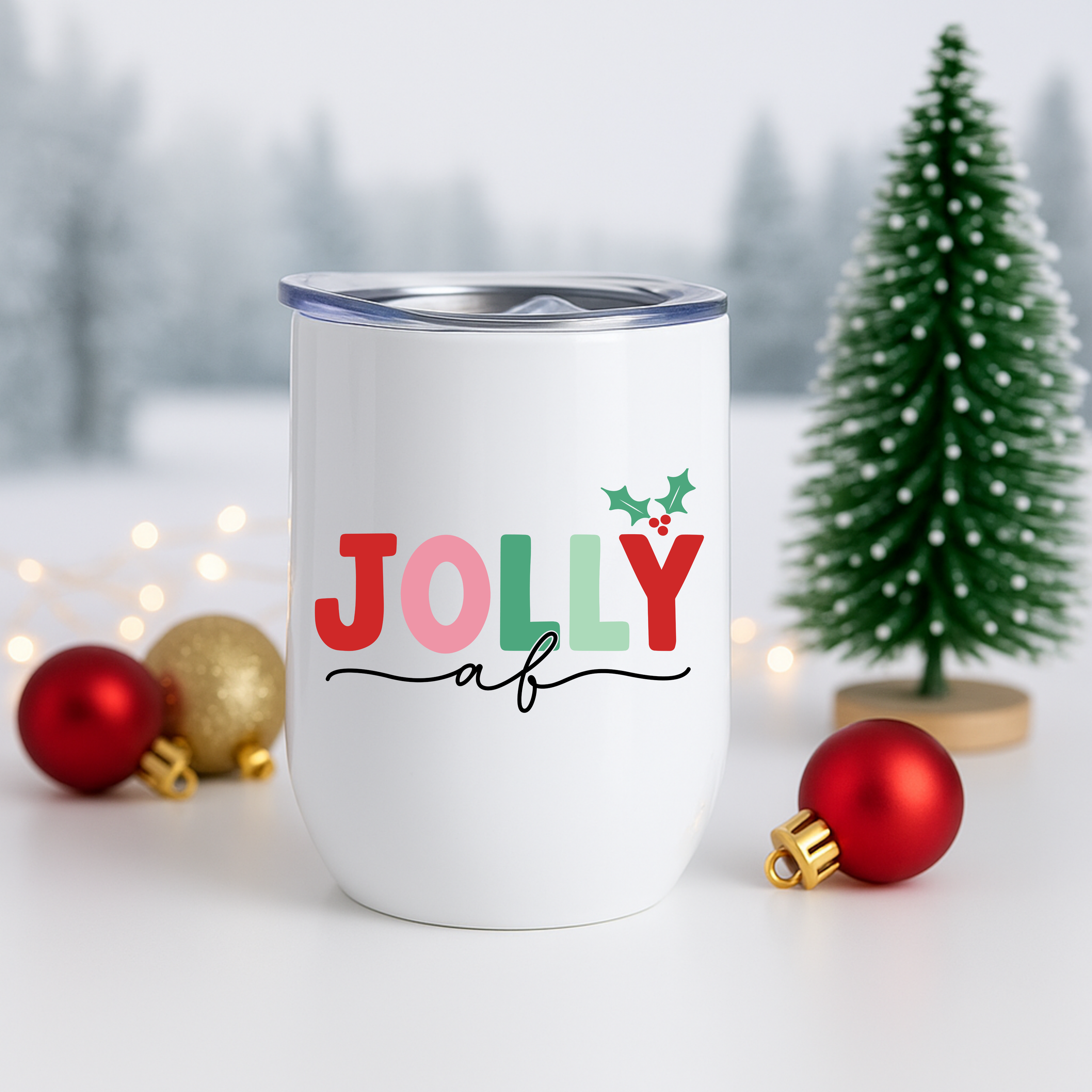 White Jolly AF tumbler shown with Christmas ornaments and a decorated mini tree.