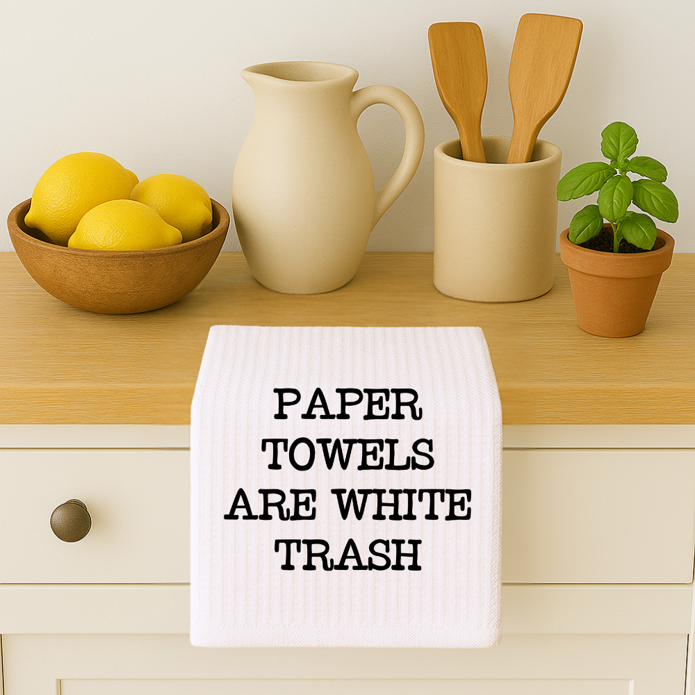 Microfiber kitchen towel hanging on a white cabinet with lemons, utensils, and a plant. Features the phrase “Paper Towels Are White Trash.”