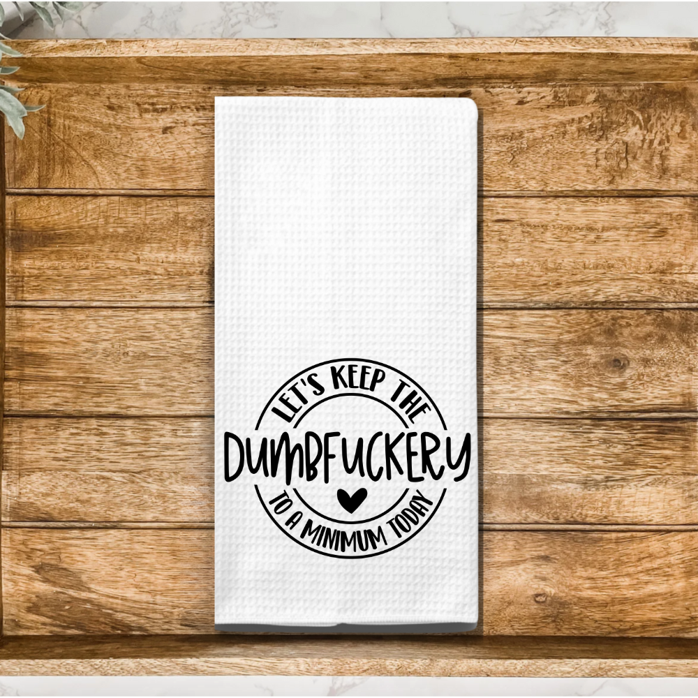 Wooden farmhouse-style kitchen background with a quirky microfiber dish towel featuring a humorous saying.