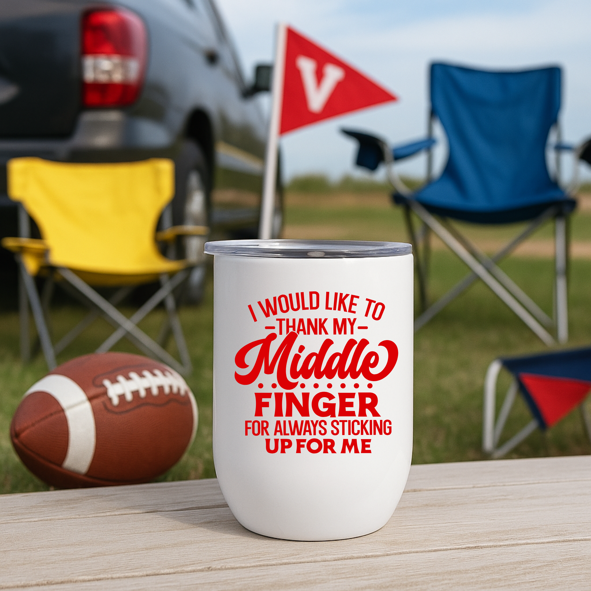 White wine tumbler with red bold font, set on a wooden table at a tailgate with football and chairs.