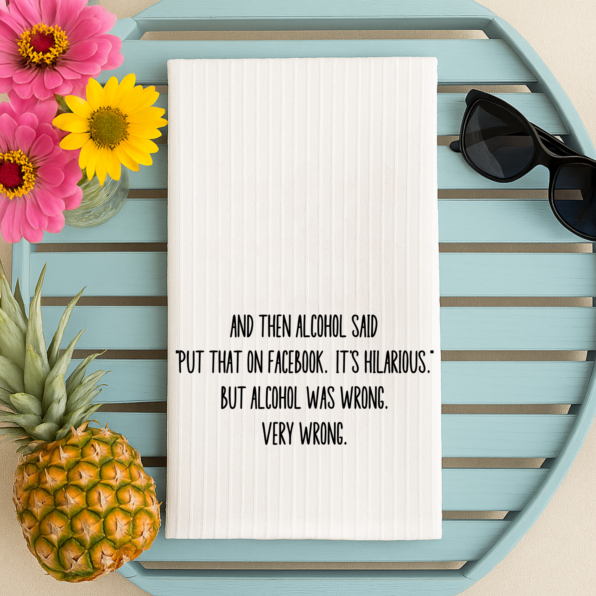 Wine lover kitchen towel with humorous quote, styled on a blue tray with sunglasses, pineapple, and flowers.