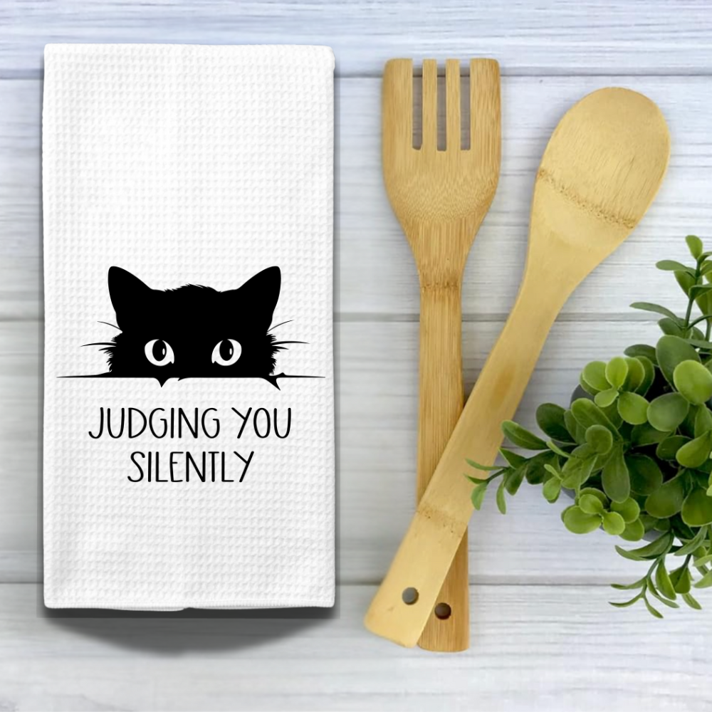 Cute cat print dish towel styled with wooden kitchen utensils and greenery on a white farmhouse-style surface. Ideal for cat mom gifts and funny kitchen decor.