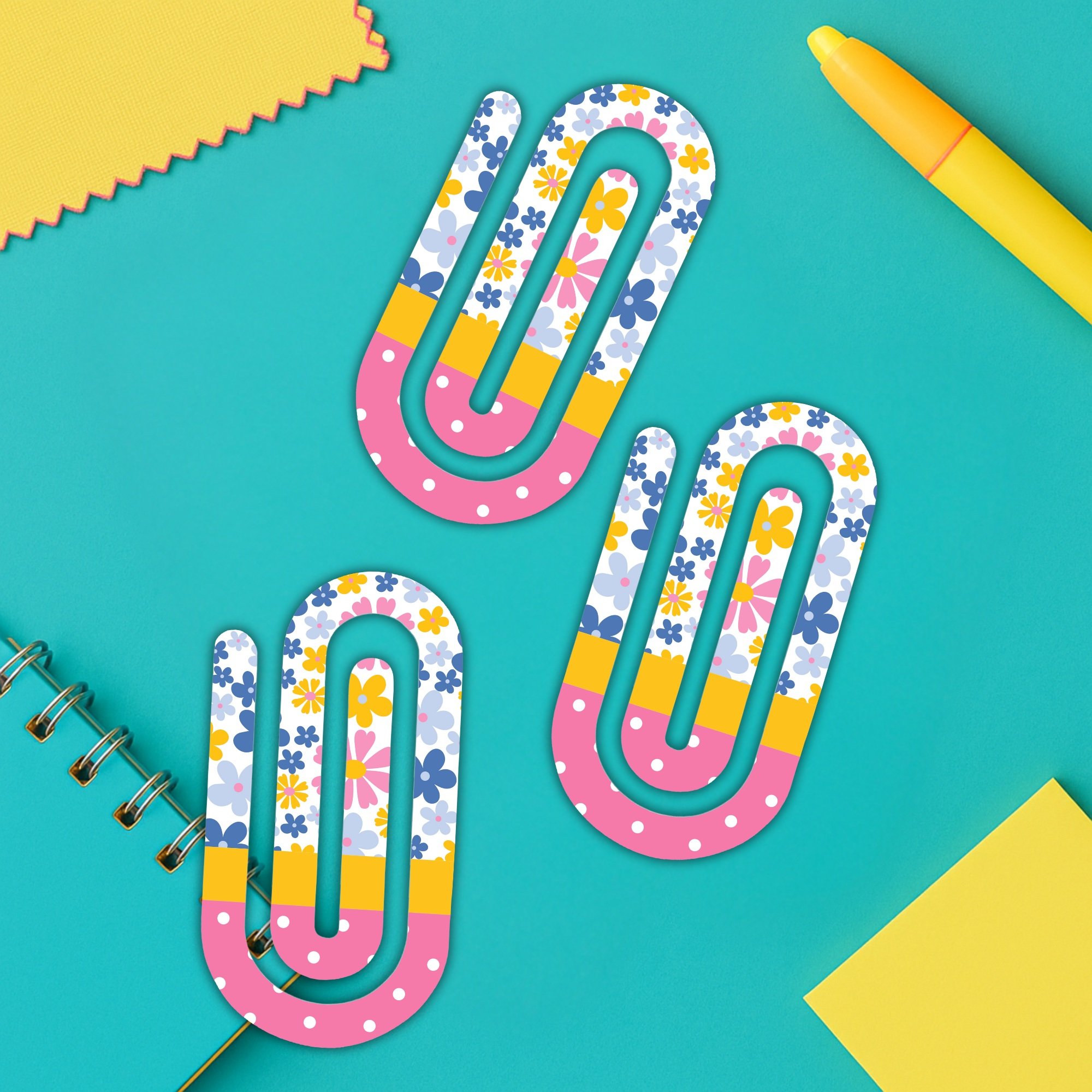 Cute floral paper clips on bright teal desk with school supplies and notebook.