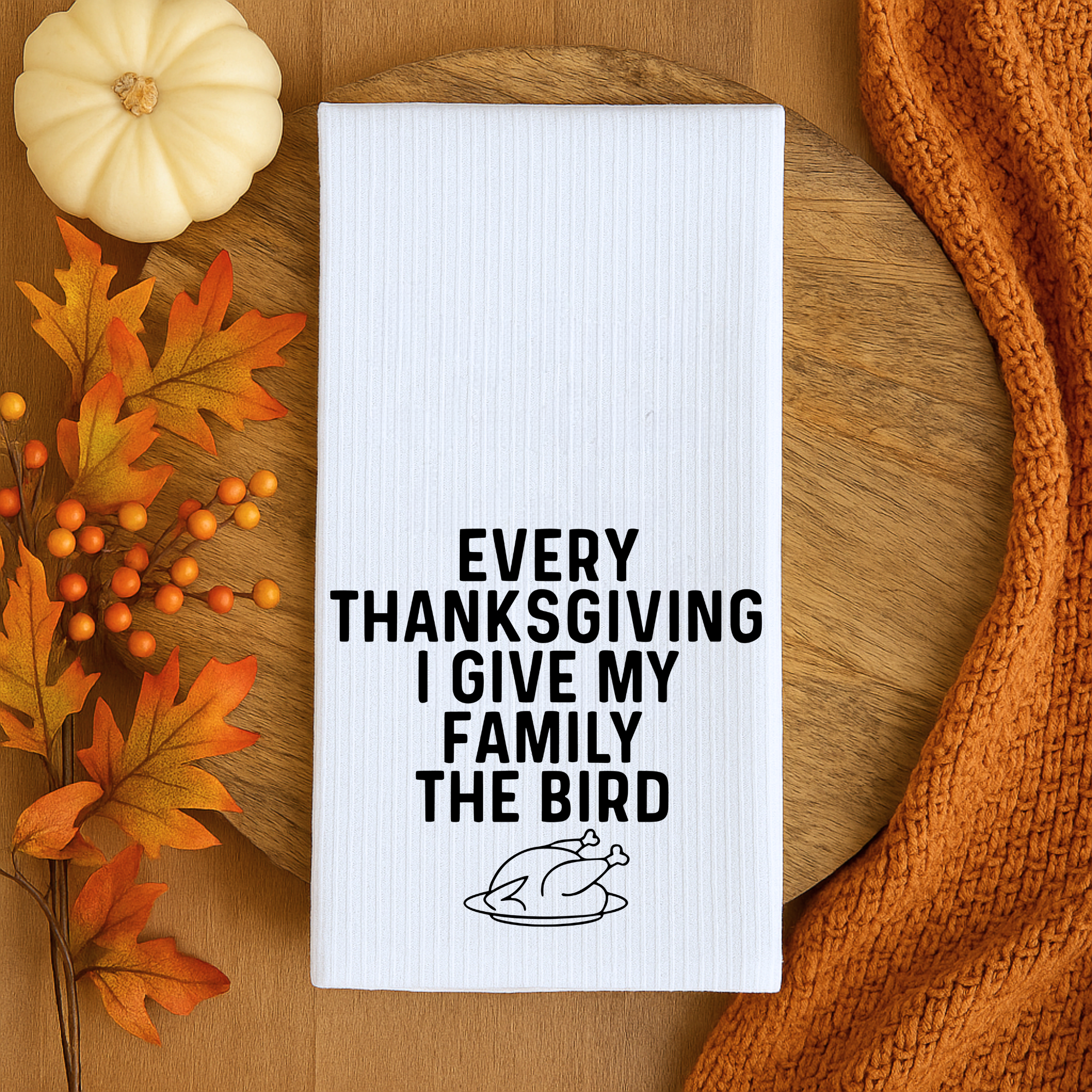 Funny Thanksgiving dish towel on a wooden tray with pumpkins and autumn leaves, featuring the quote “Every Thanksgiving I Give My Family the Bird.”