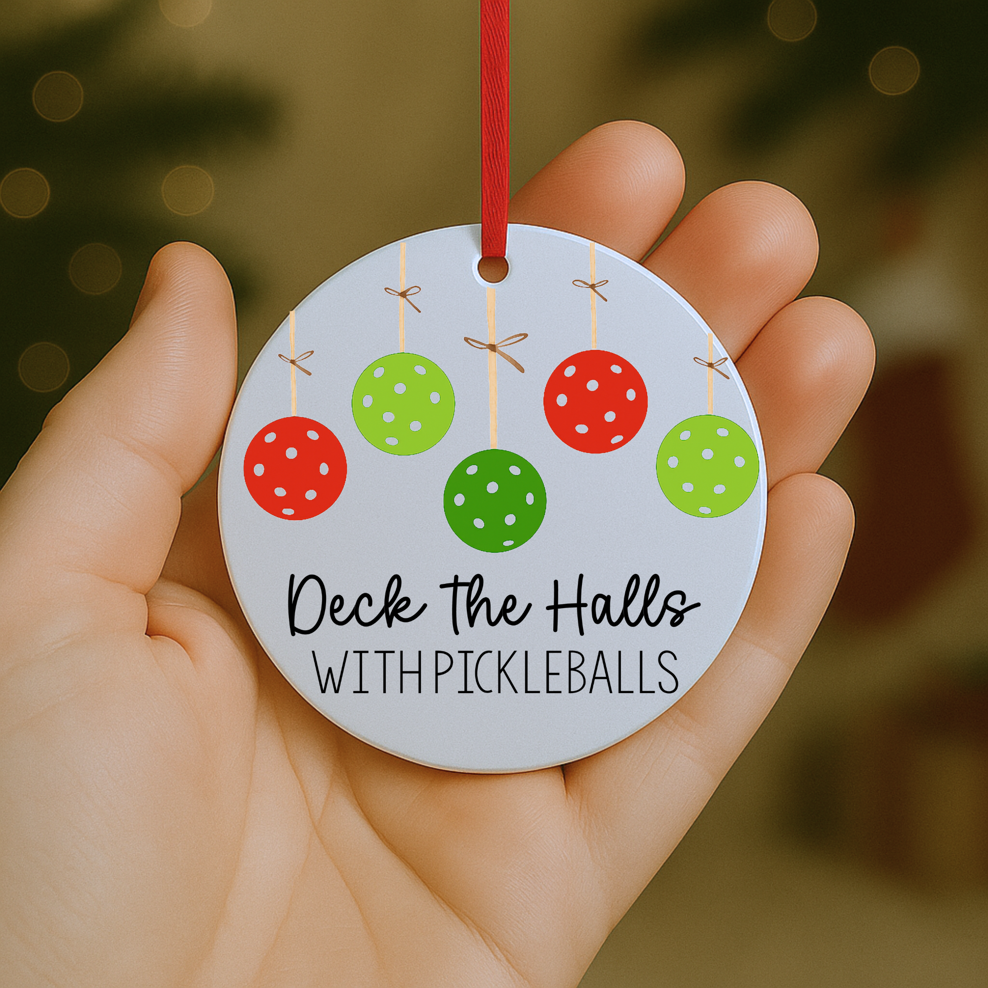 “Hand holding a festive pickleball Christmas ornament with colorful pickleball baubles and ‘Deck the Halls with Pickleballs’ lettering.”