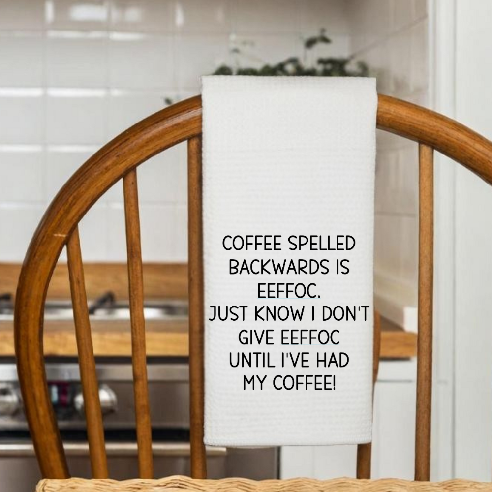 White waffle weave dish towel featuring a coffee humor quote, draped over a rustic wooden chair in a cozy kitchen.