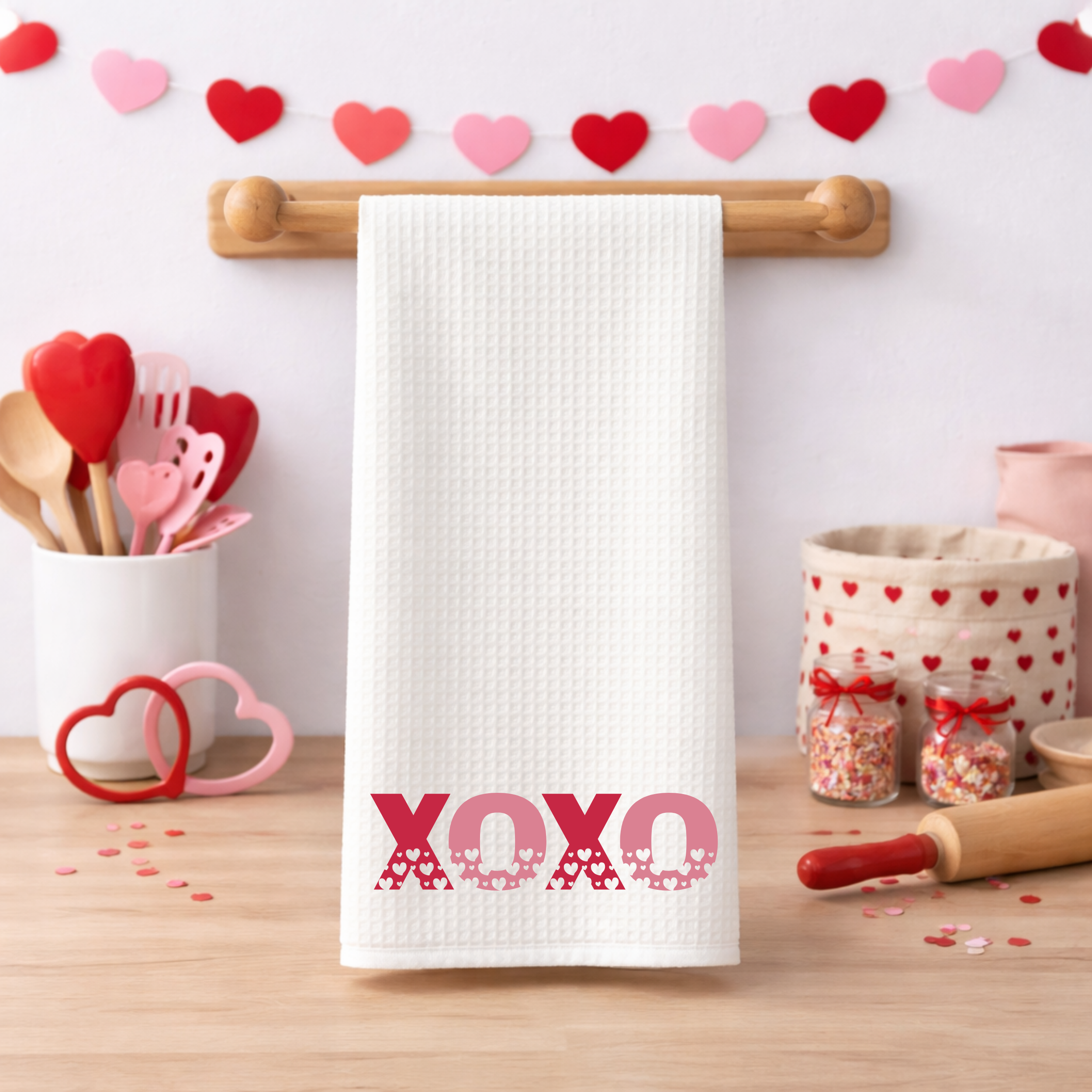 XOXO Valentine’s Day dish towel hanging beneath heart garland in bright kitchen setting