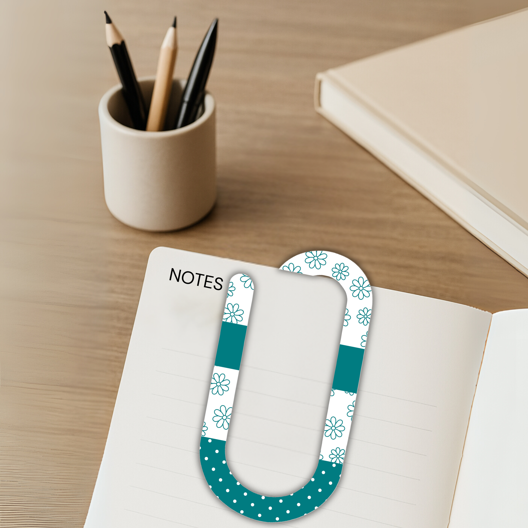 Oversized acrylic paperclip clipped onto a notes page with pencils and modern desk decor.