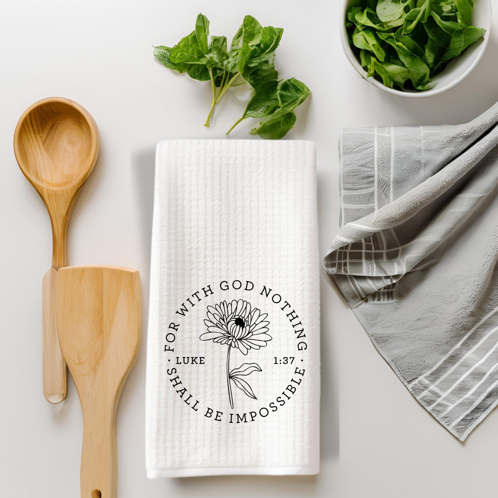 Christian scripture towel flat-lay styled with wooden spoons, greens, and gray linens on a white kitchen surface.