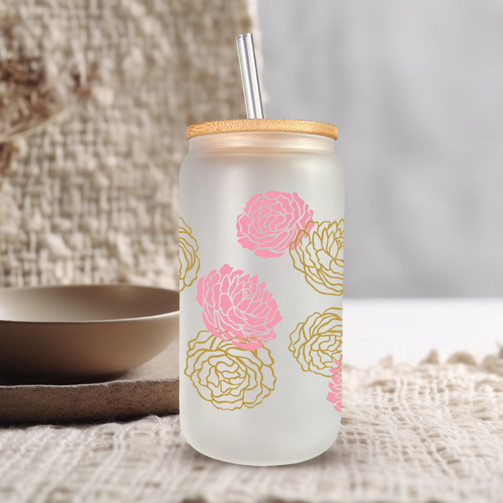 Reusable floral frosted glass tumbler with bamboo lid and straw on cozy textured surface.