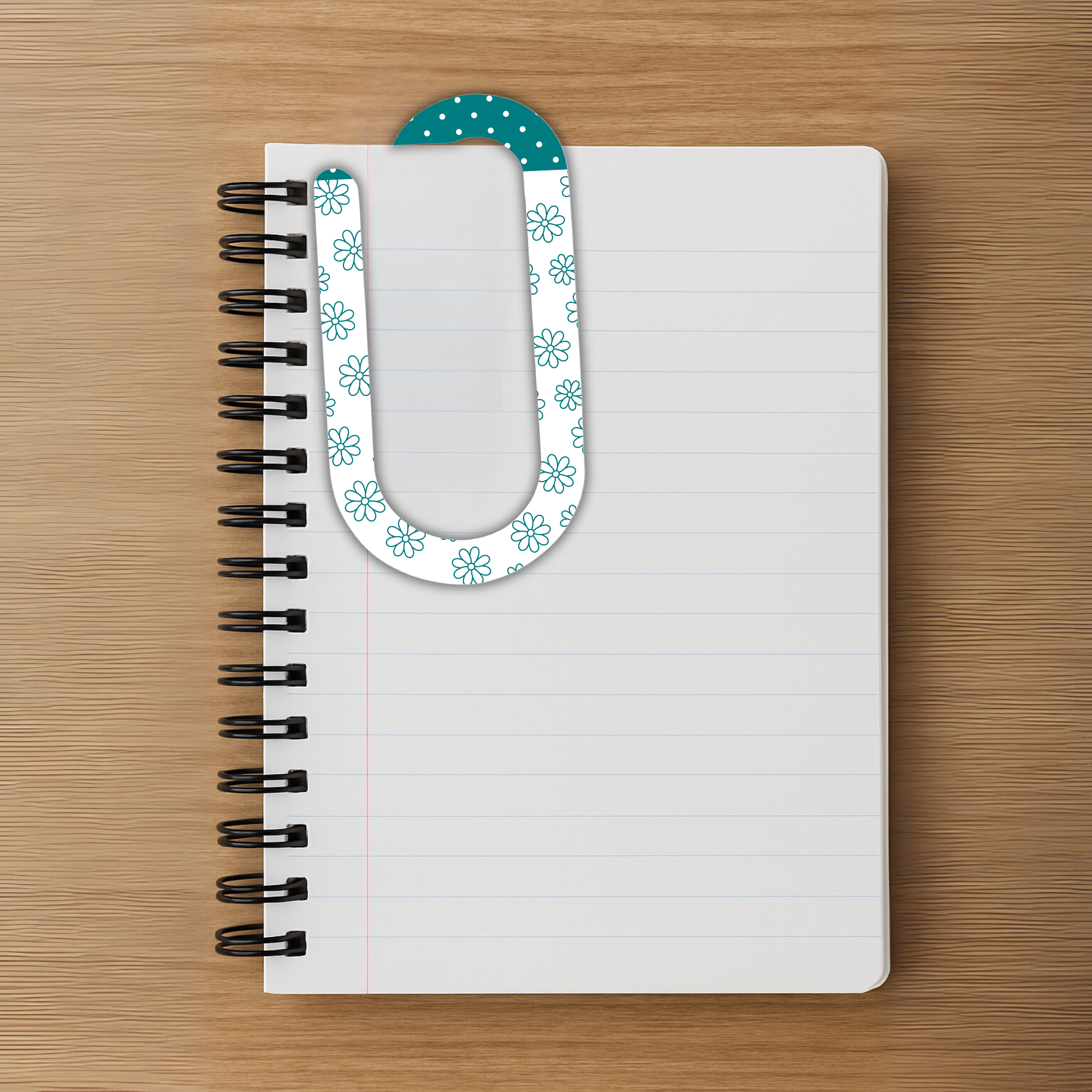 Oversized floral acrylic paperclip holding pages in a spiral notebook on a wood surface.