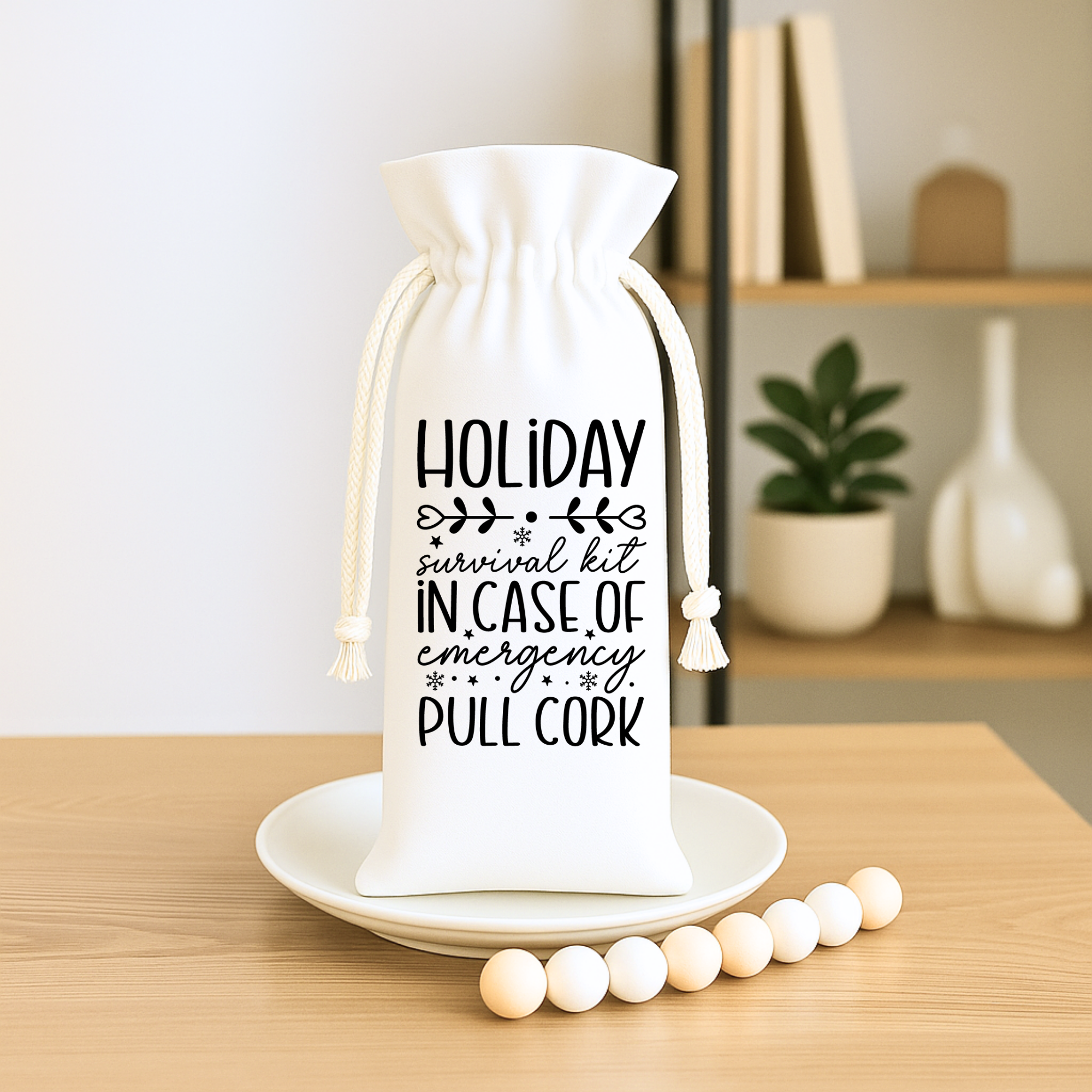 White drawstring wine bag featuring the quote “Holiday Survival Kit – In Case of Emergency Pull Cork,” styled with wooden beads.