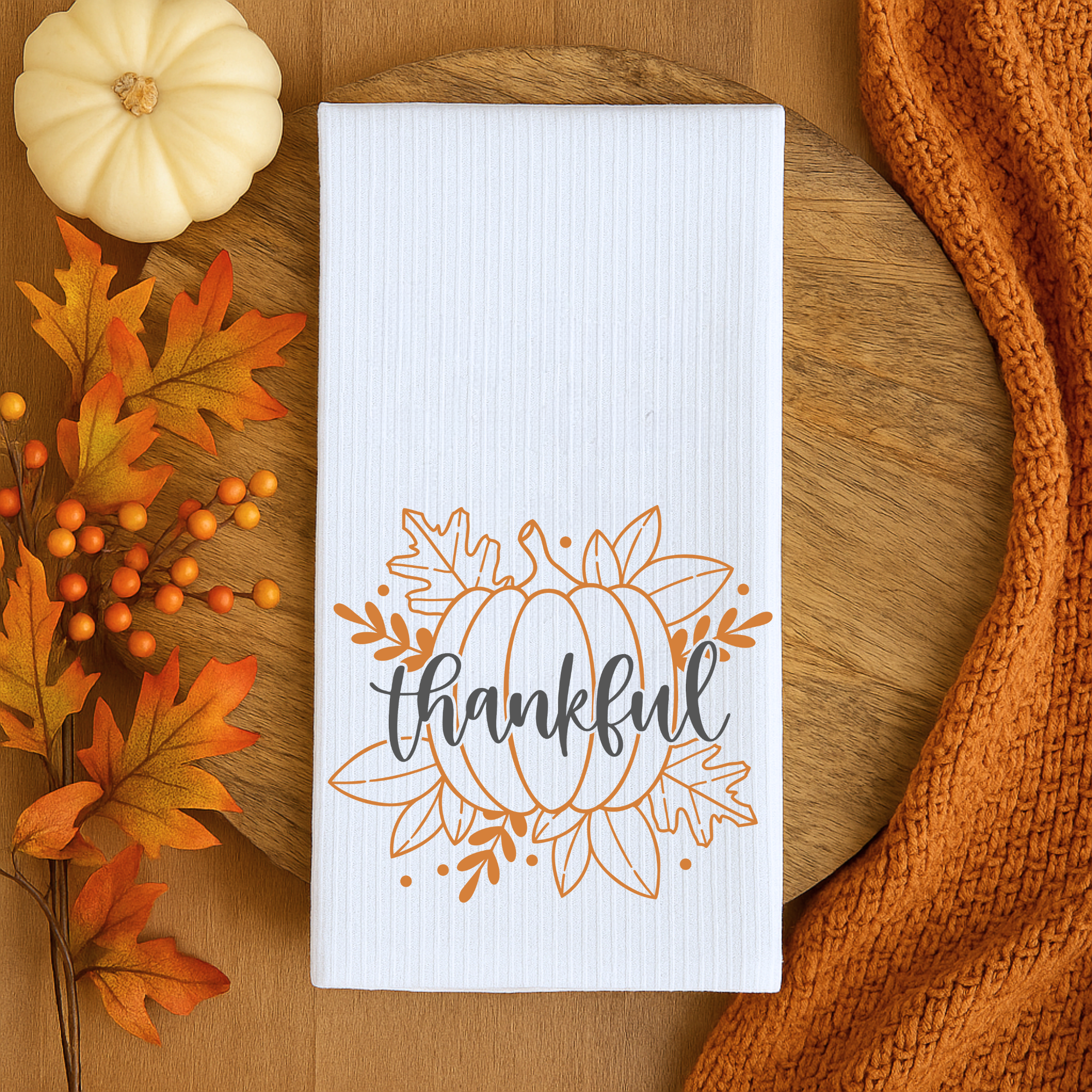 Thanksgiving dish towel with pumpkin design and thankful lettering on wooden board.