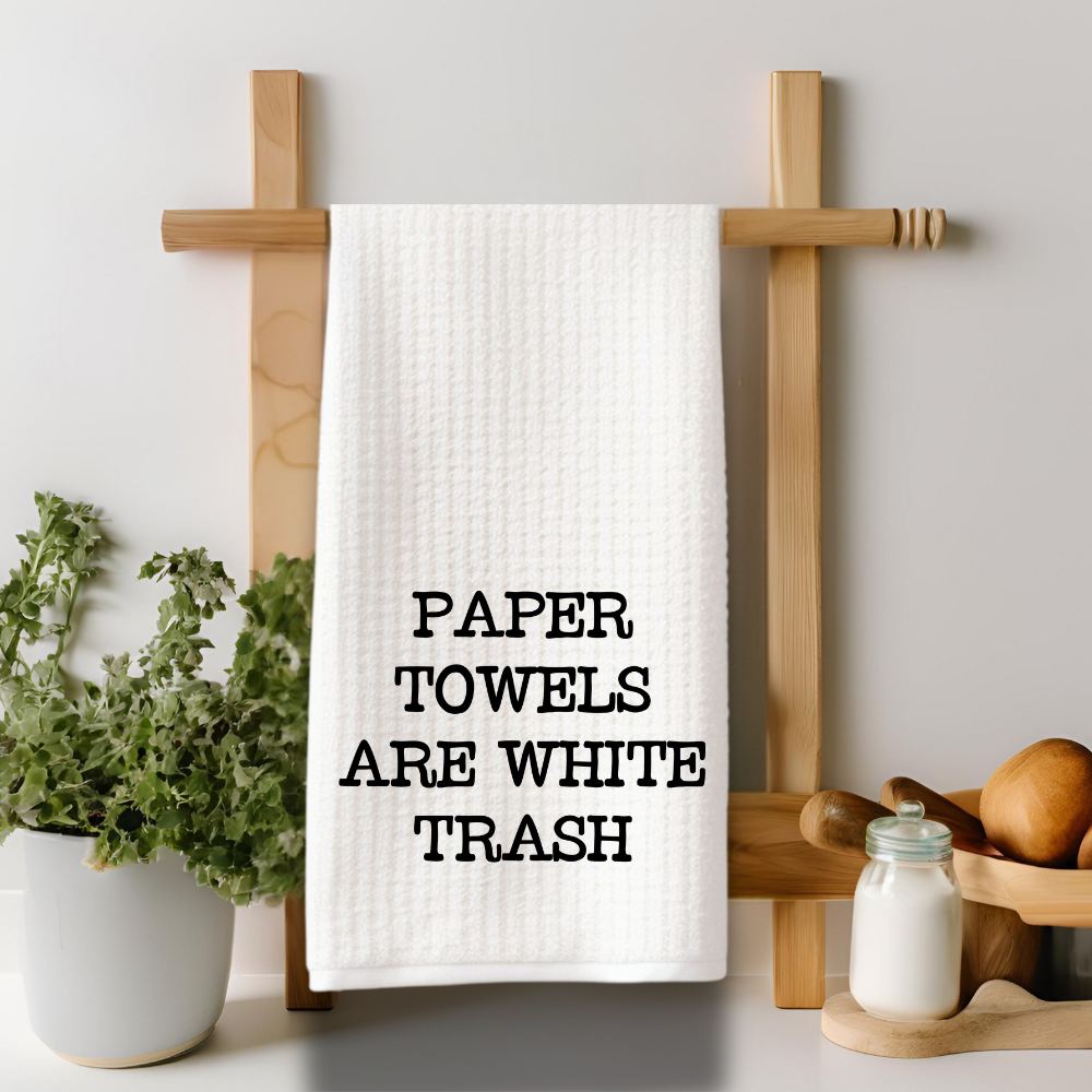 Reusable microfiber kitchen towel with the phrase “Paper Towels Are White Trash” hanging on a rustic wooden towel rack.