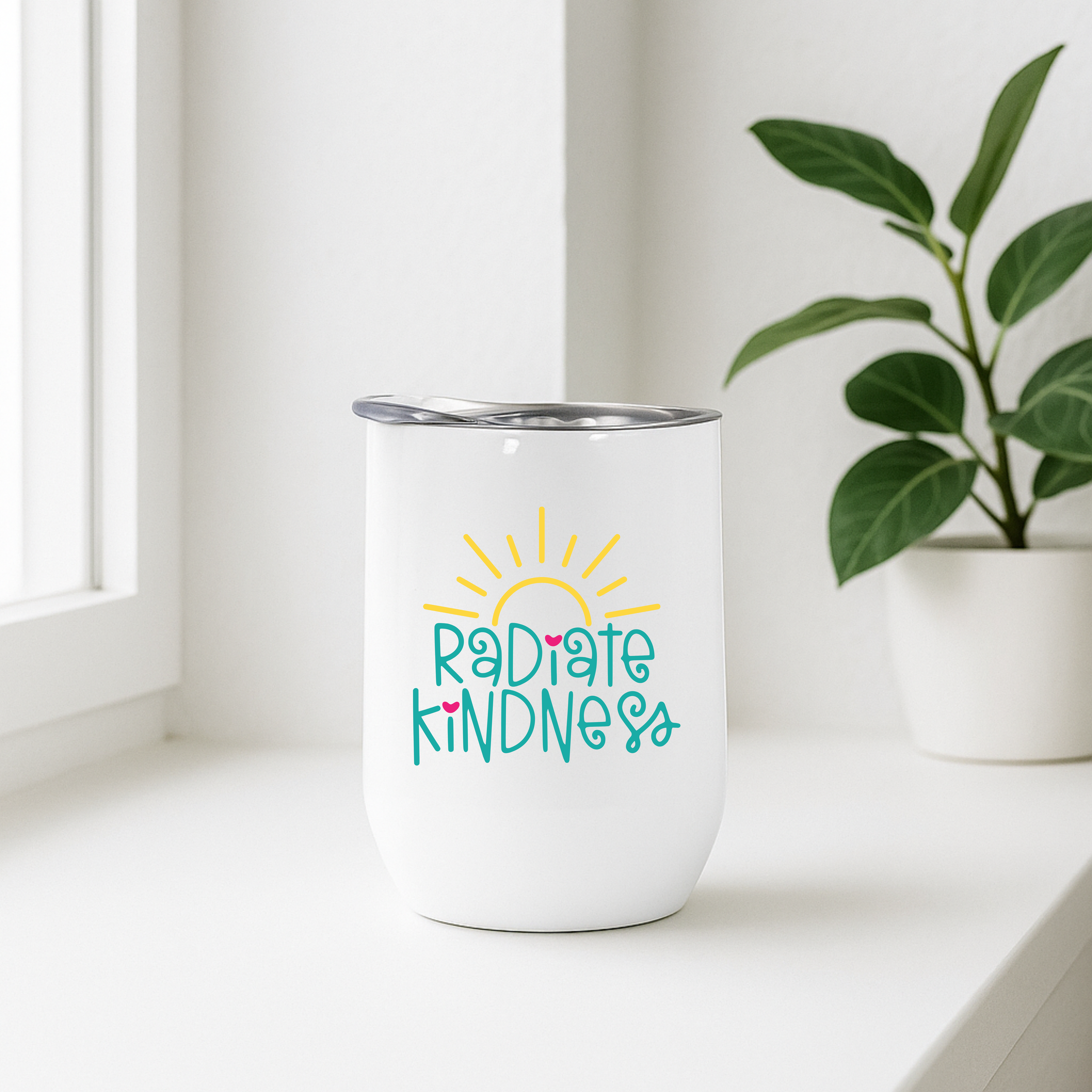 Radiate Kindness insulated wine tumbler on a bright windowsill with a potted plant