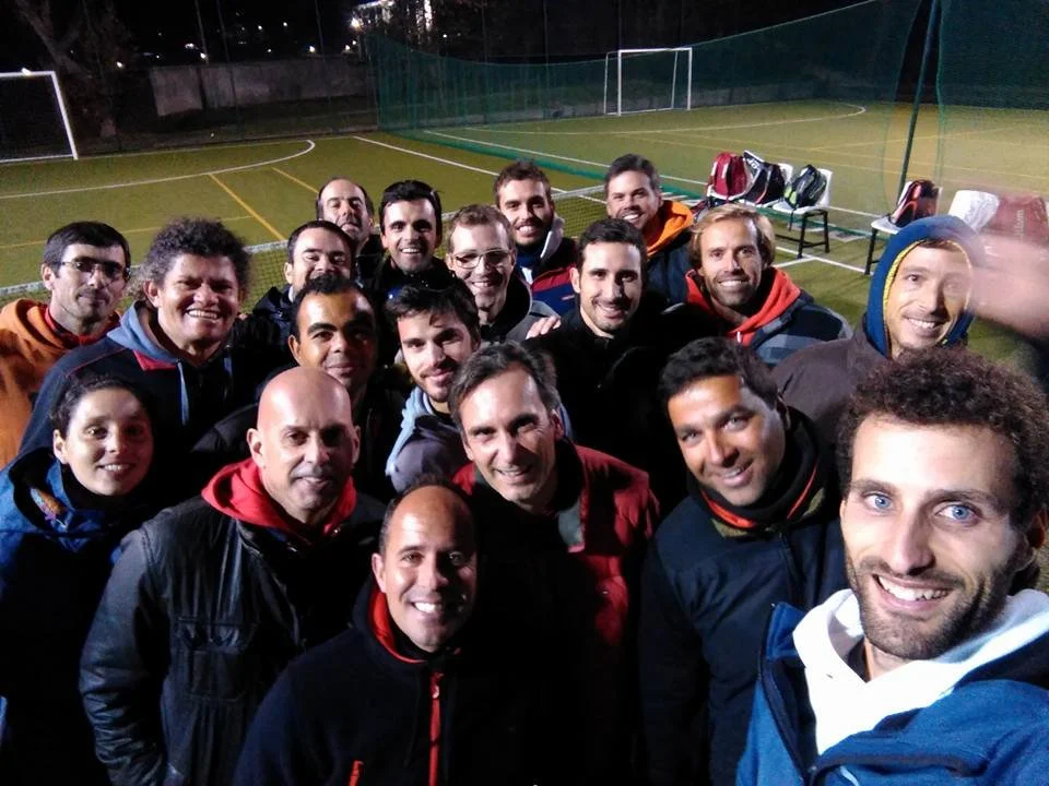 Group of people on a soccer field at night, taking a selfie, with a goalpost and nets in the background.