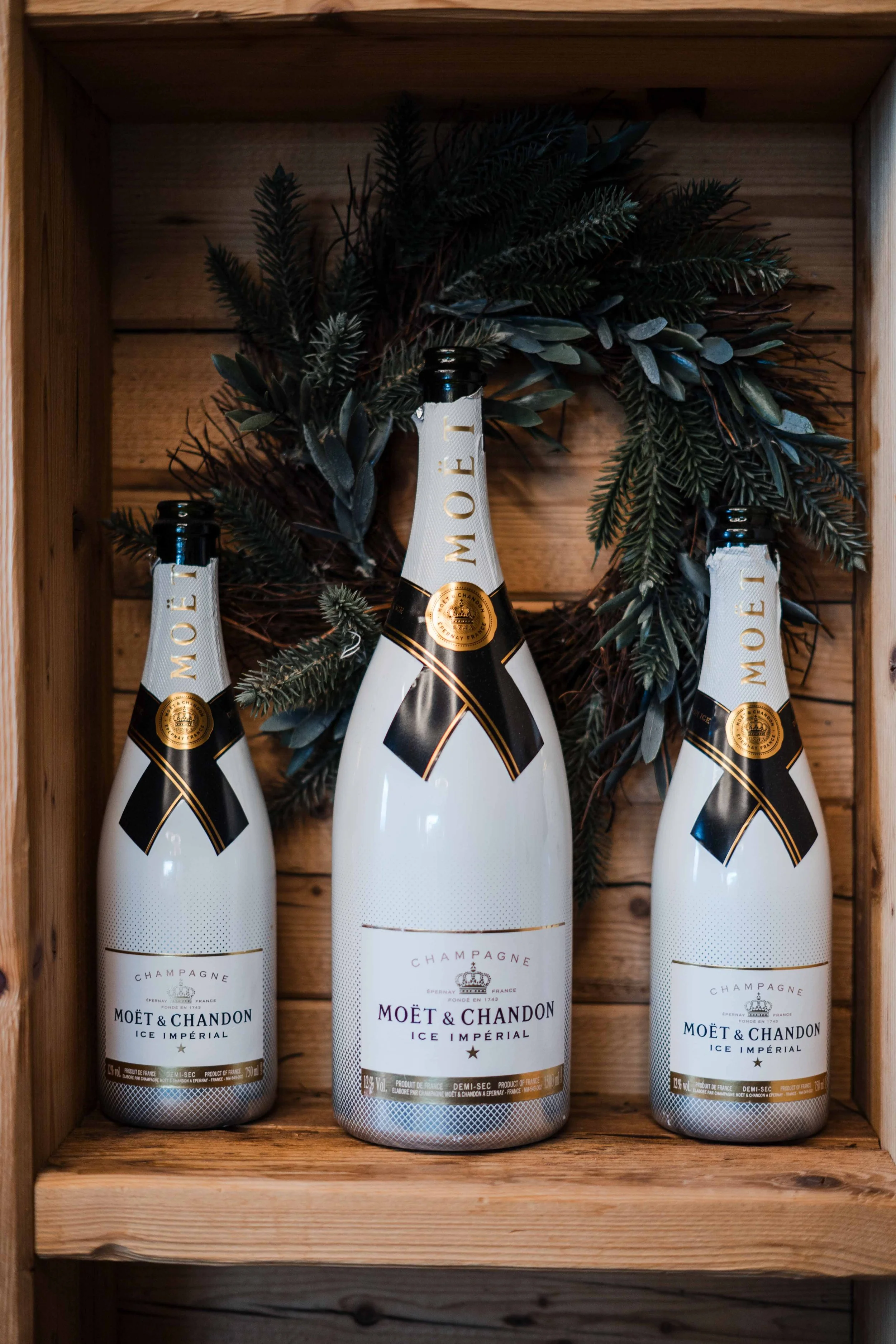 Drei Flaschen Moët & Chandon Ice Imperial Champagner in einer Holzregal mit Tannenzweigen im Hintergrund.