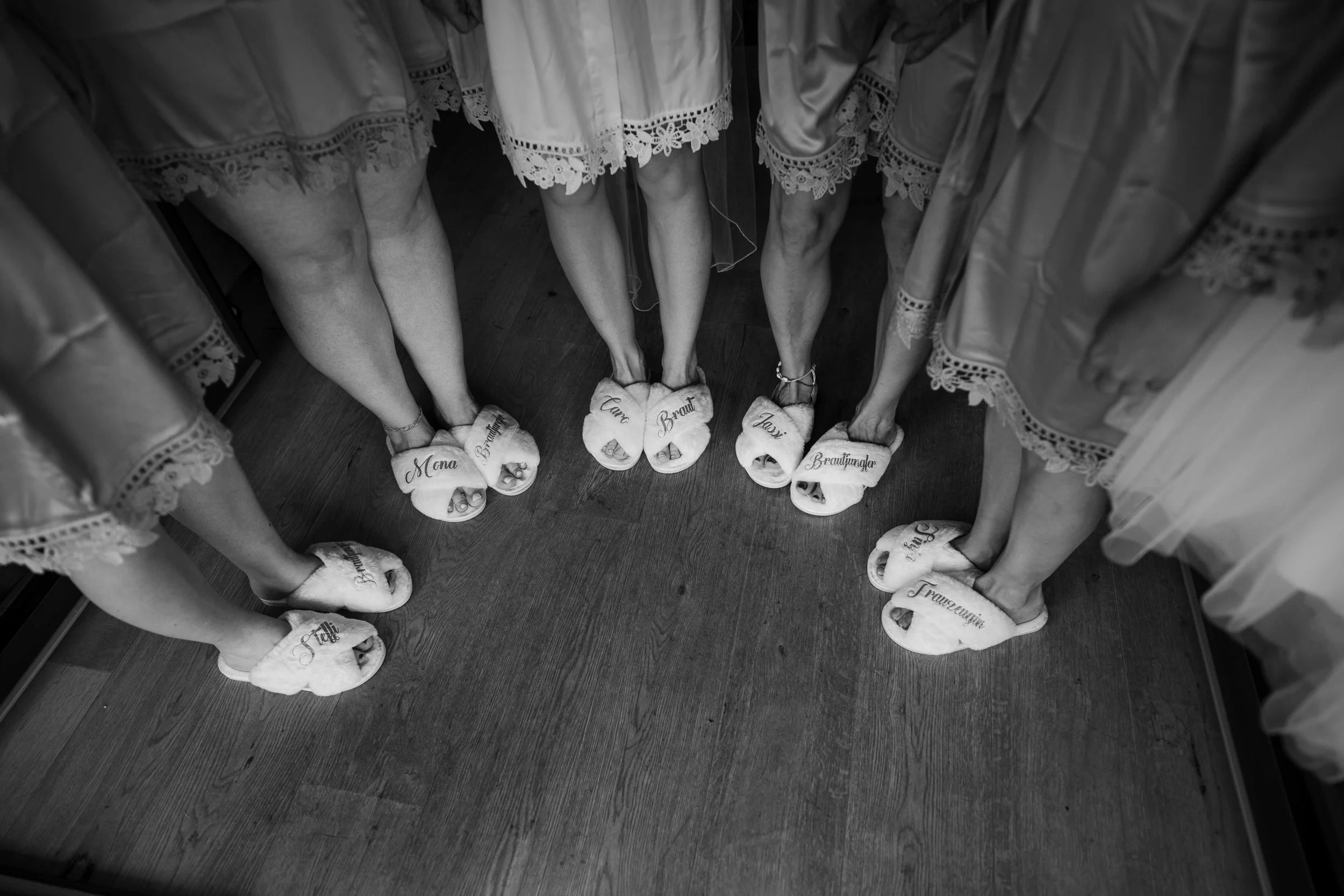 Frauengruppe in Brautschränken, die auf Holzboden stehen, mit weißen Badhandschuhen mit schwarzen Aufschriften am Boden, die ihre Schuhe bedecken.