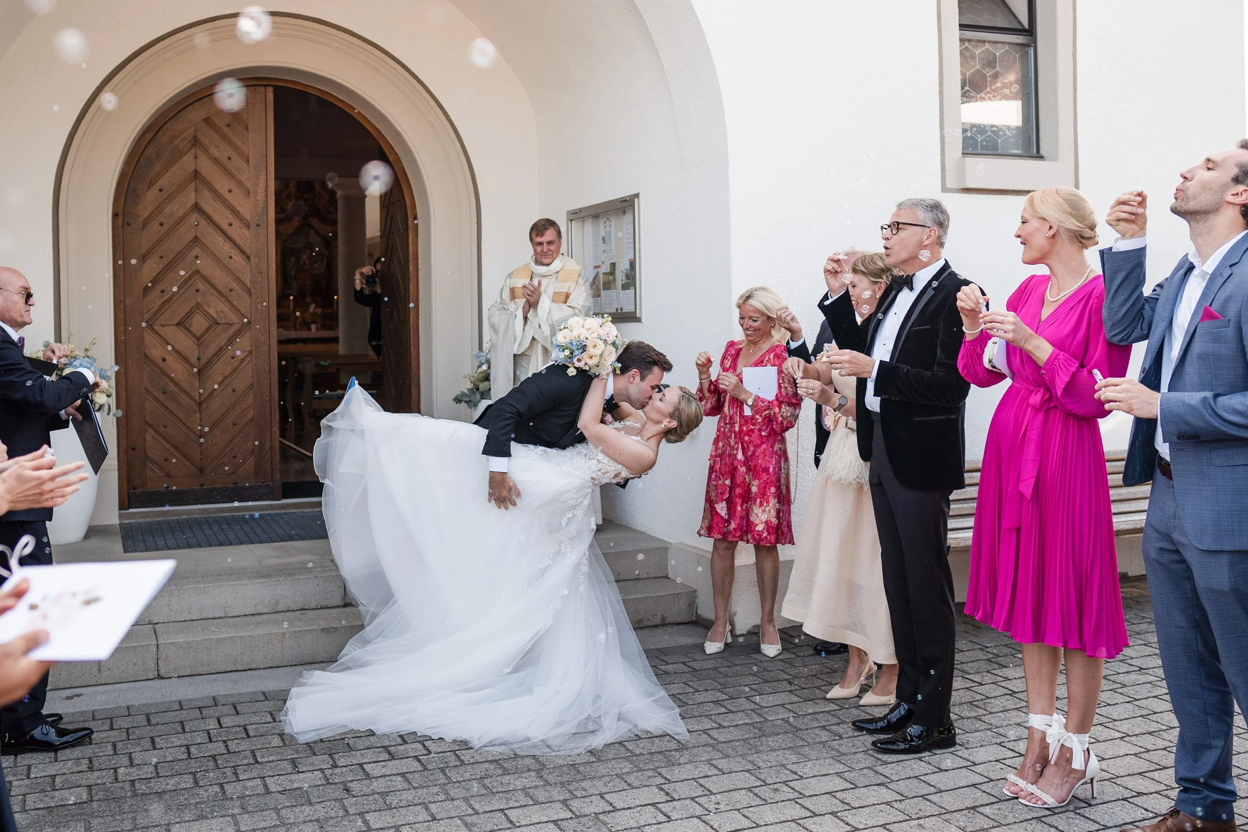 Hochzeitspaar küsst sich vor versammelter Hochzeitsgesellschaft vor der Kirche