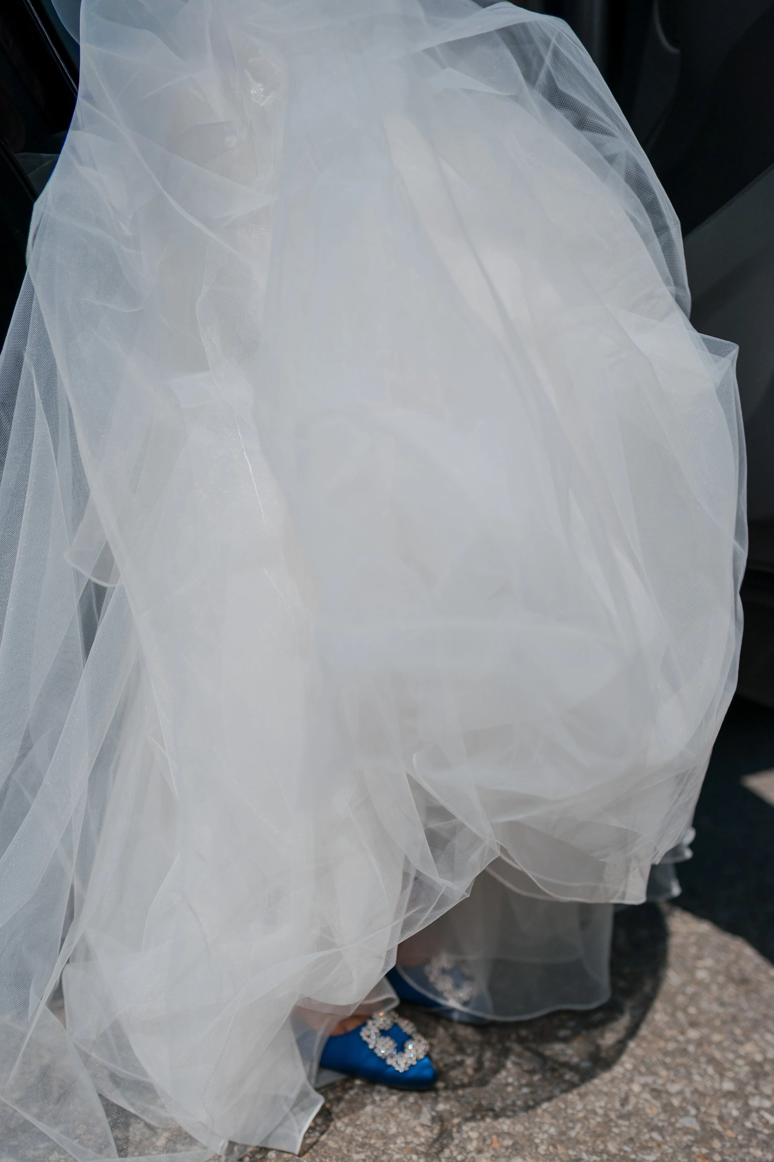 Braut in Hochzeitskleid und blauen Schuhen mit Schmuck, im Auto sitzend.