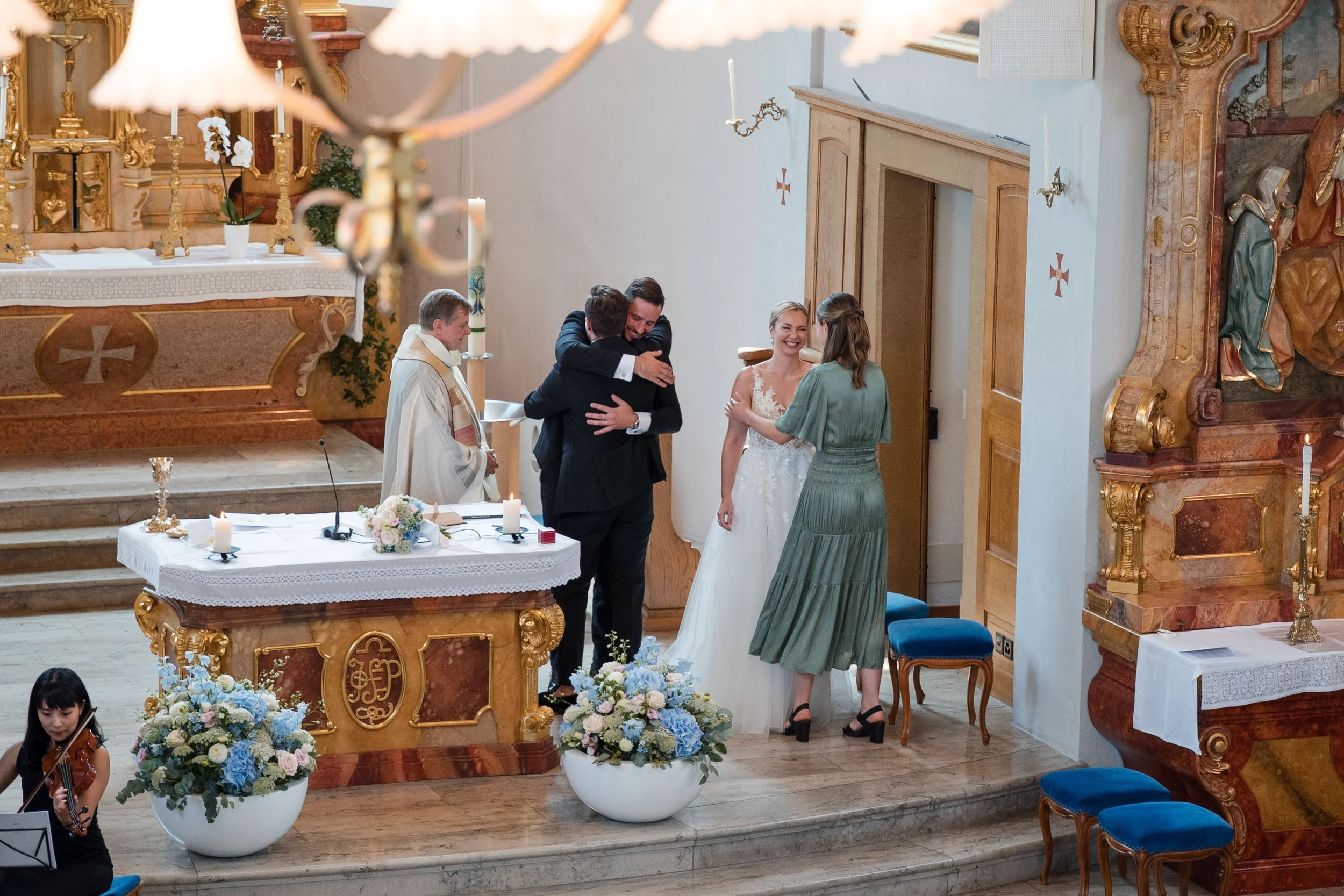 Hochzeitszeremonie in einer Kirche mit Brautpaar, Pfarrer und Gästen, die sich umarmen