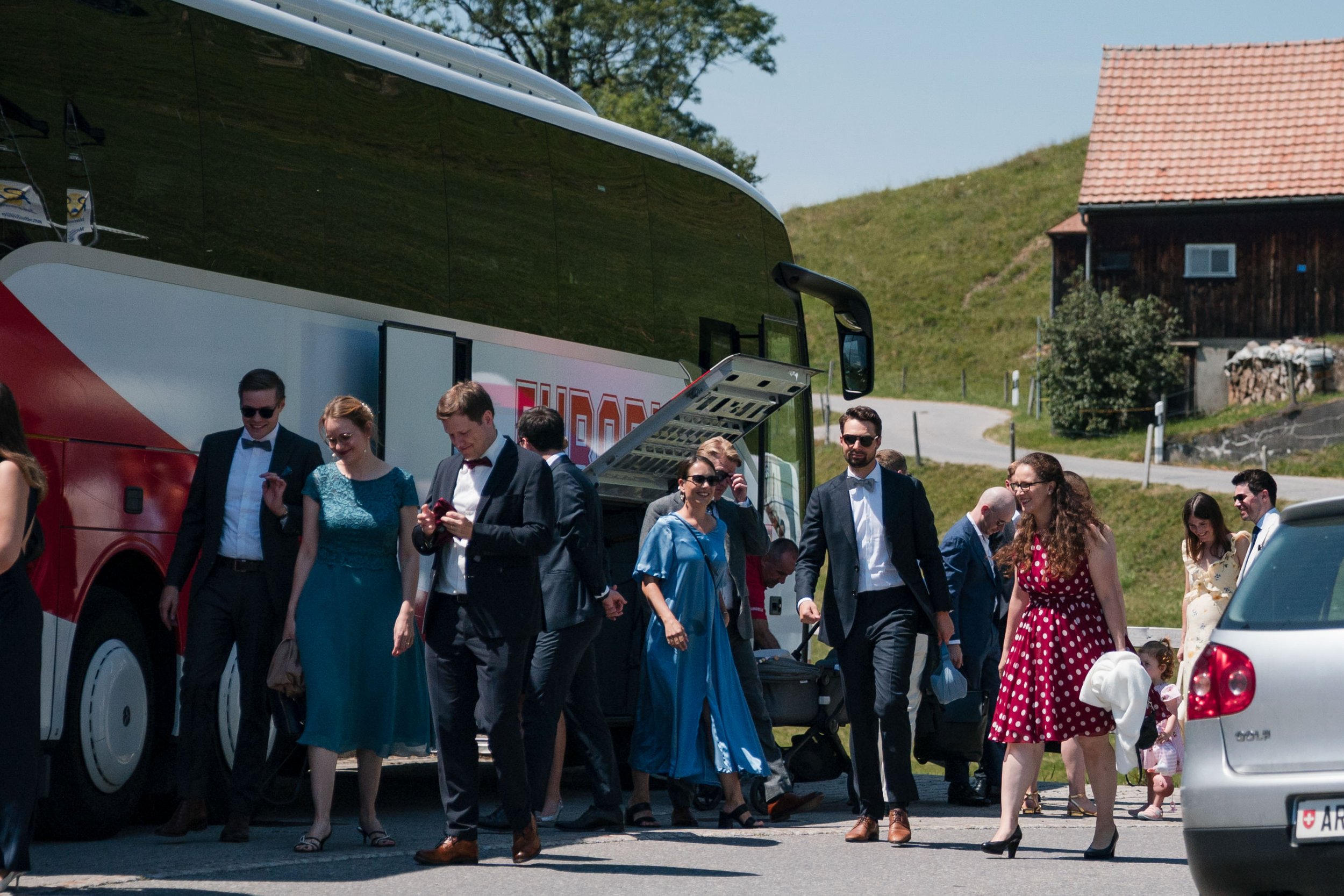 Menschen in formeller Kleidung steigen aus einem Bus auf dem Land, auf einem sonnigen Tag.