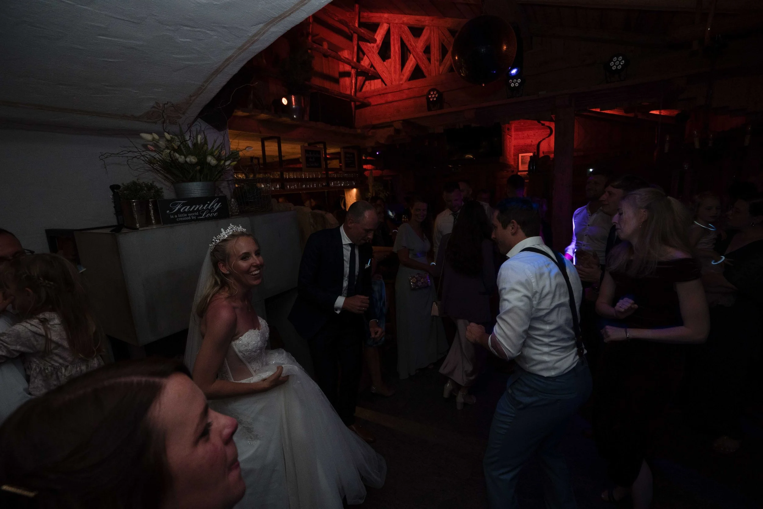 Hochzeitspaar beim Tanzen in einer dunklen, festlich dekorierten Location mit Gästen, die Spaß haben.