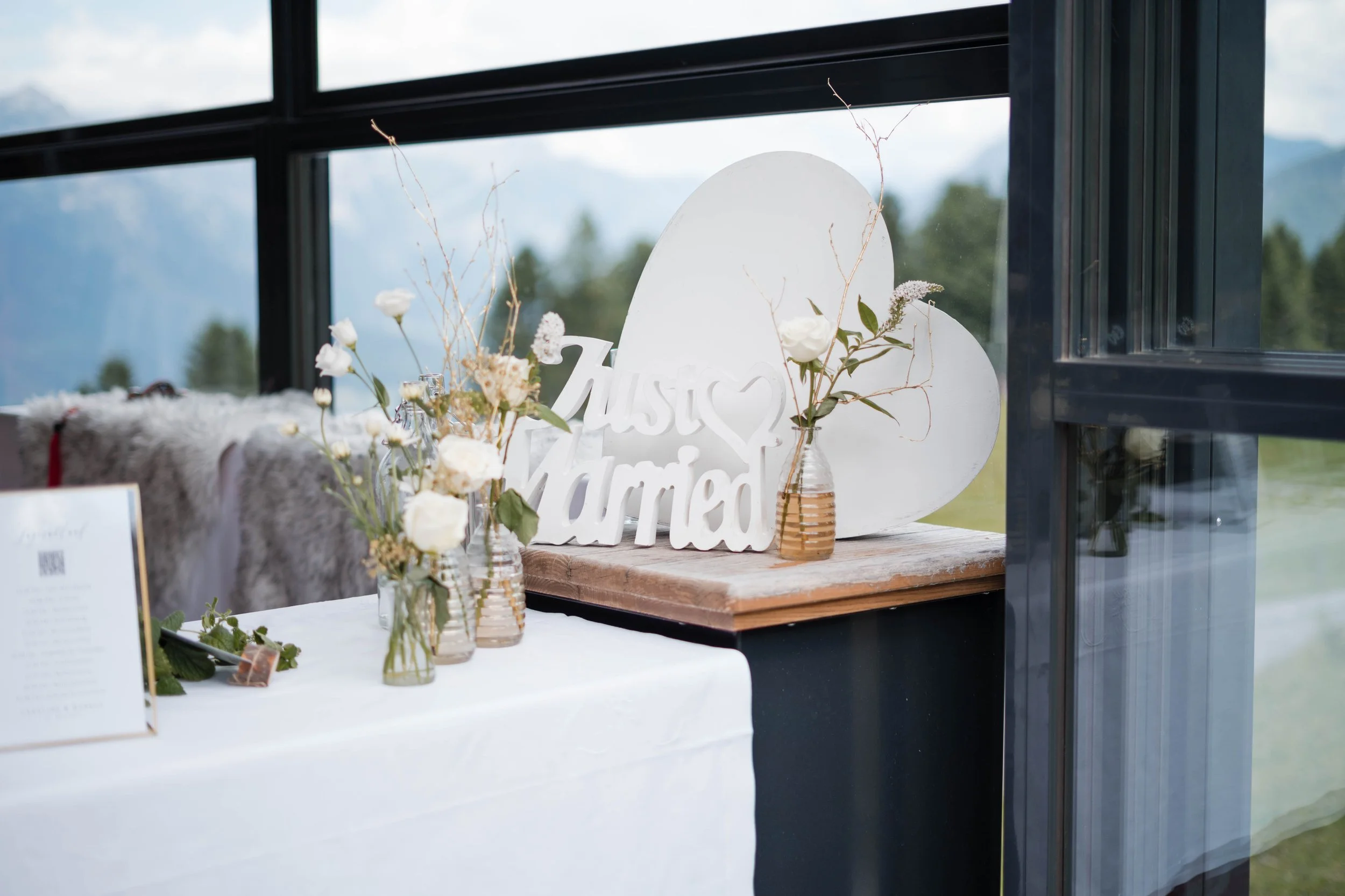 Blumenarrangement mit weißen Rosen und Dekorationen auf einem Tisch, mit einer Schlagschrift 'Unser Wunder' im Hintergrund.