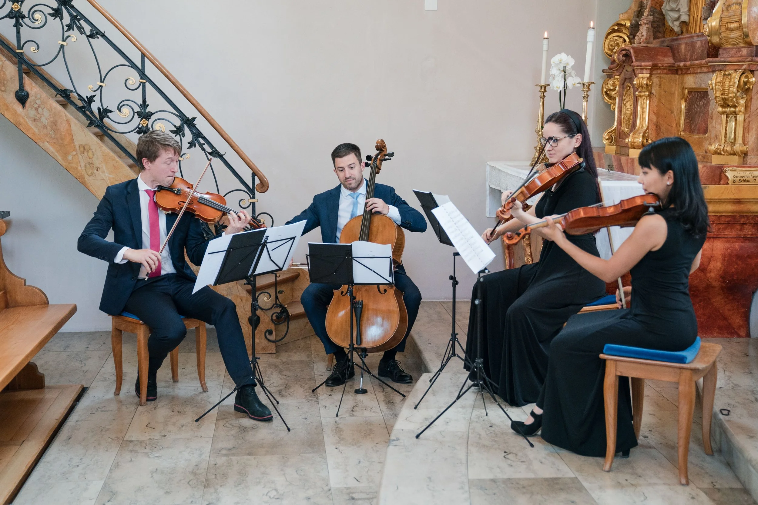 Vier Musiker spielen klassische Musik in einer Kirche, mit Stühlen, Notenständern und einem Altar im Hintergrund.