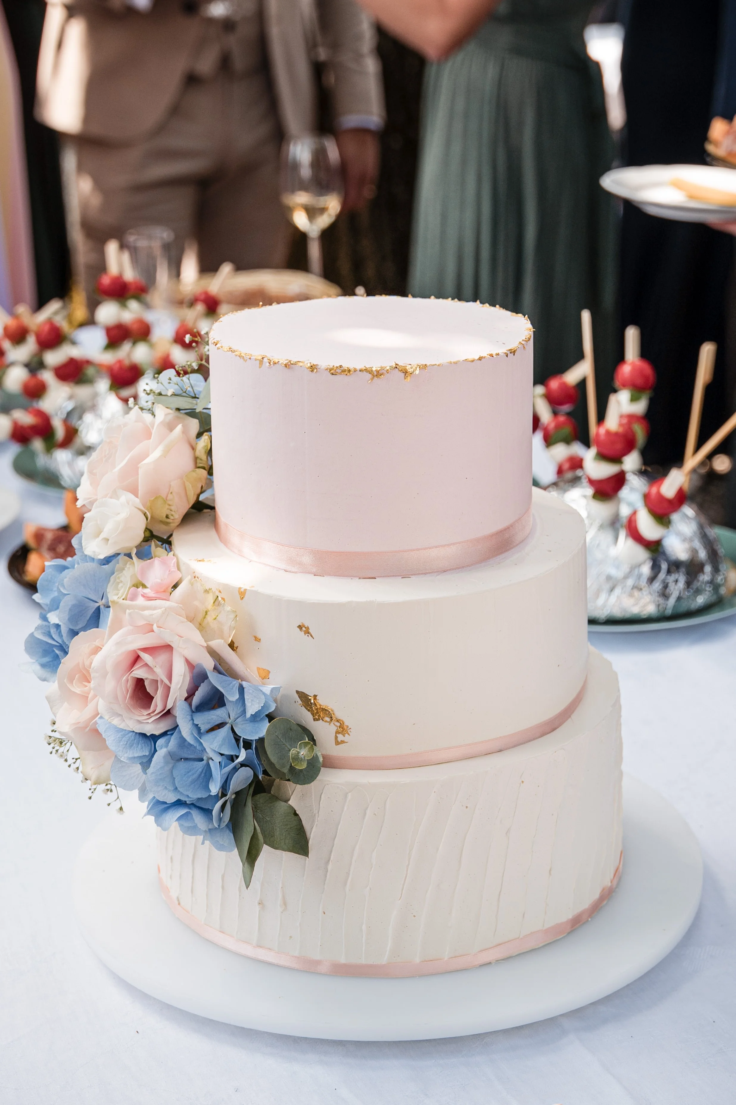Drei-stöckige Hochzeitstorte mit weißen und pinkfarbenen Verzierung und Frischeblumen, auf einem weißen Teller
