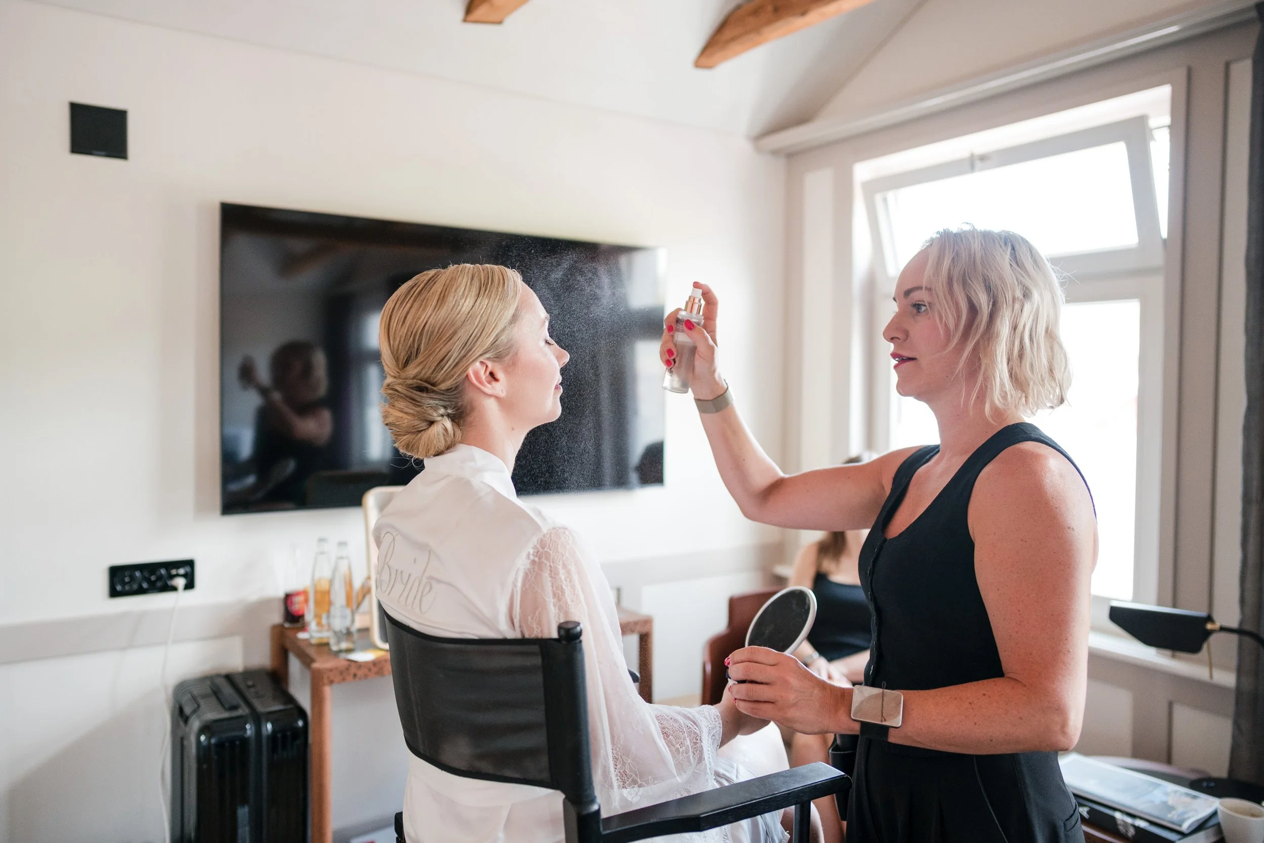 Frau sprüht Haarspray auf eine Braut, die sich für eine Hochzeit vorbereitet.
