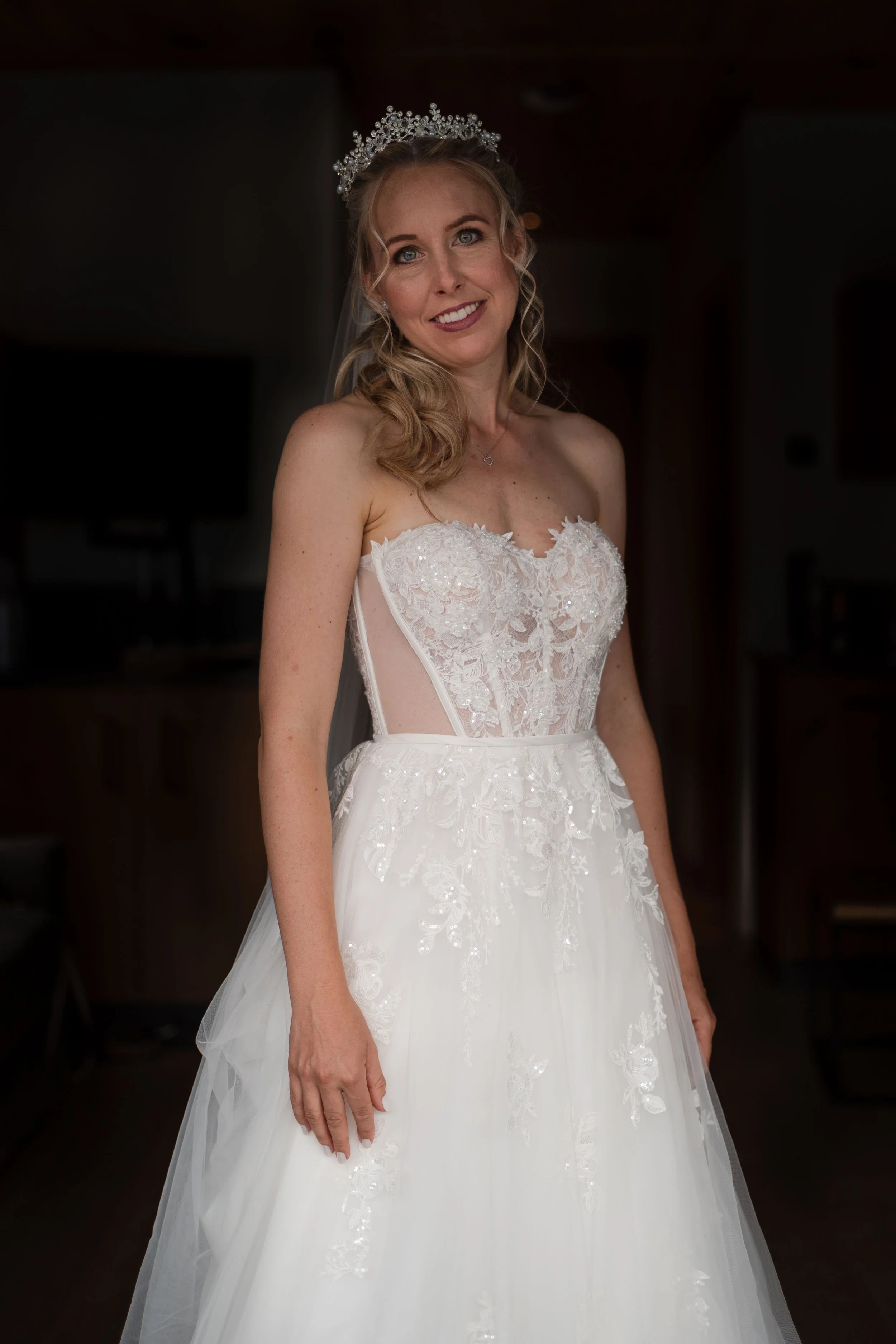 Frau in Brautkleid mit Diadem, Lächeln, blondes lockiges Haar, im Hintergrund dunkel