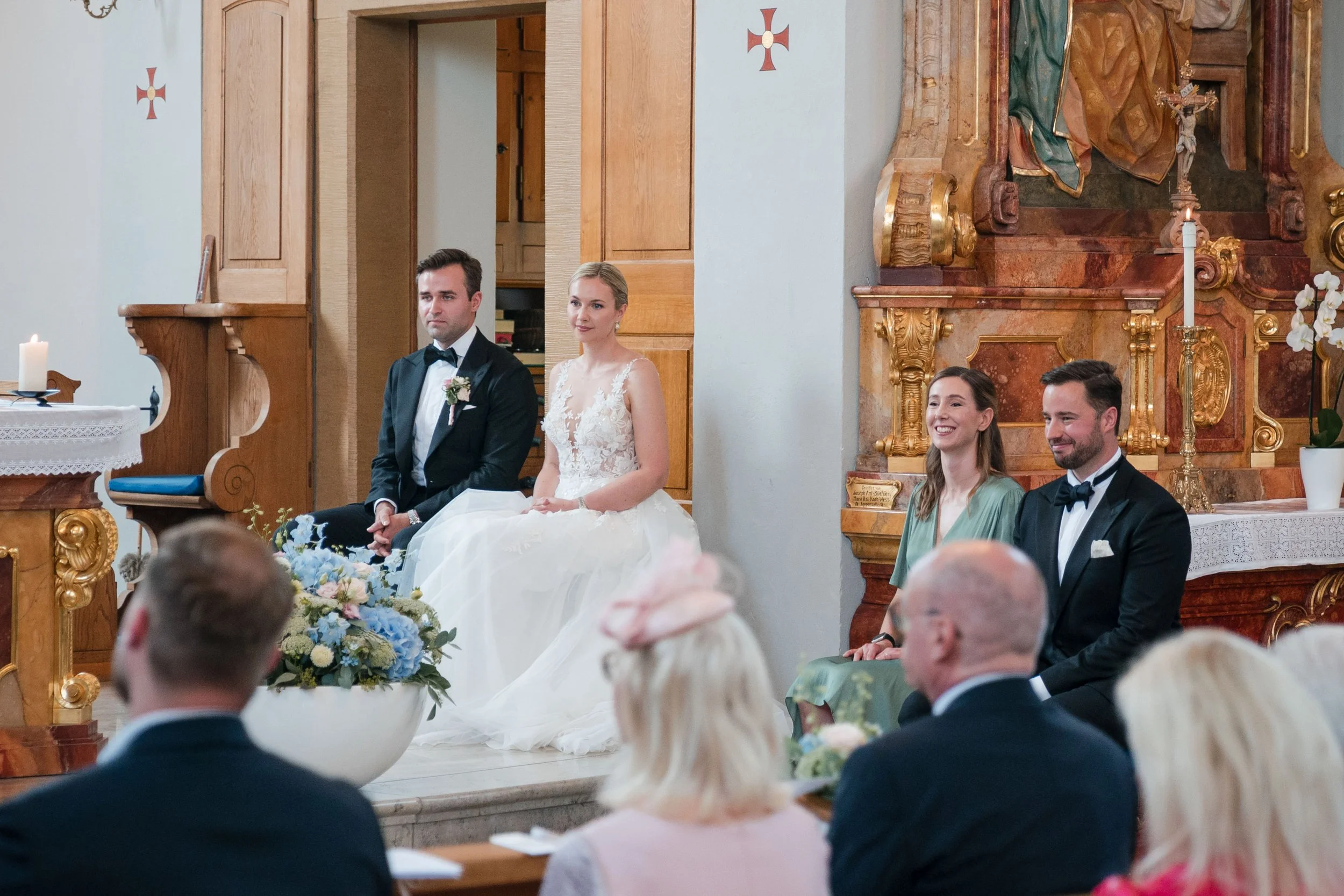 Hochzeitsszene in einer Kirche mit Hochzeitspaar und Gästen.