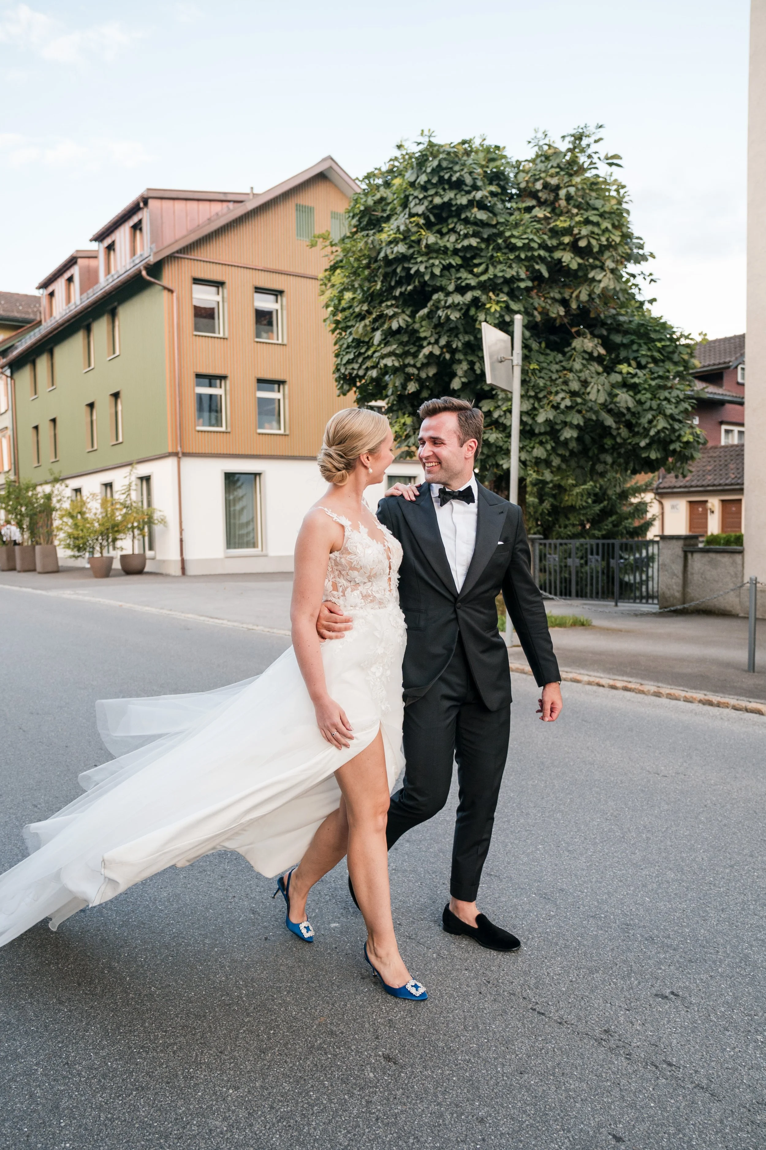 Ein glückliches Brautpaar in formeller Kleidung, die auf einer leeren Straße in einer Stadt spazieren gehen.