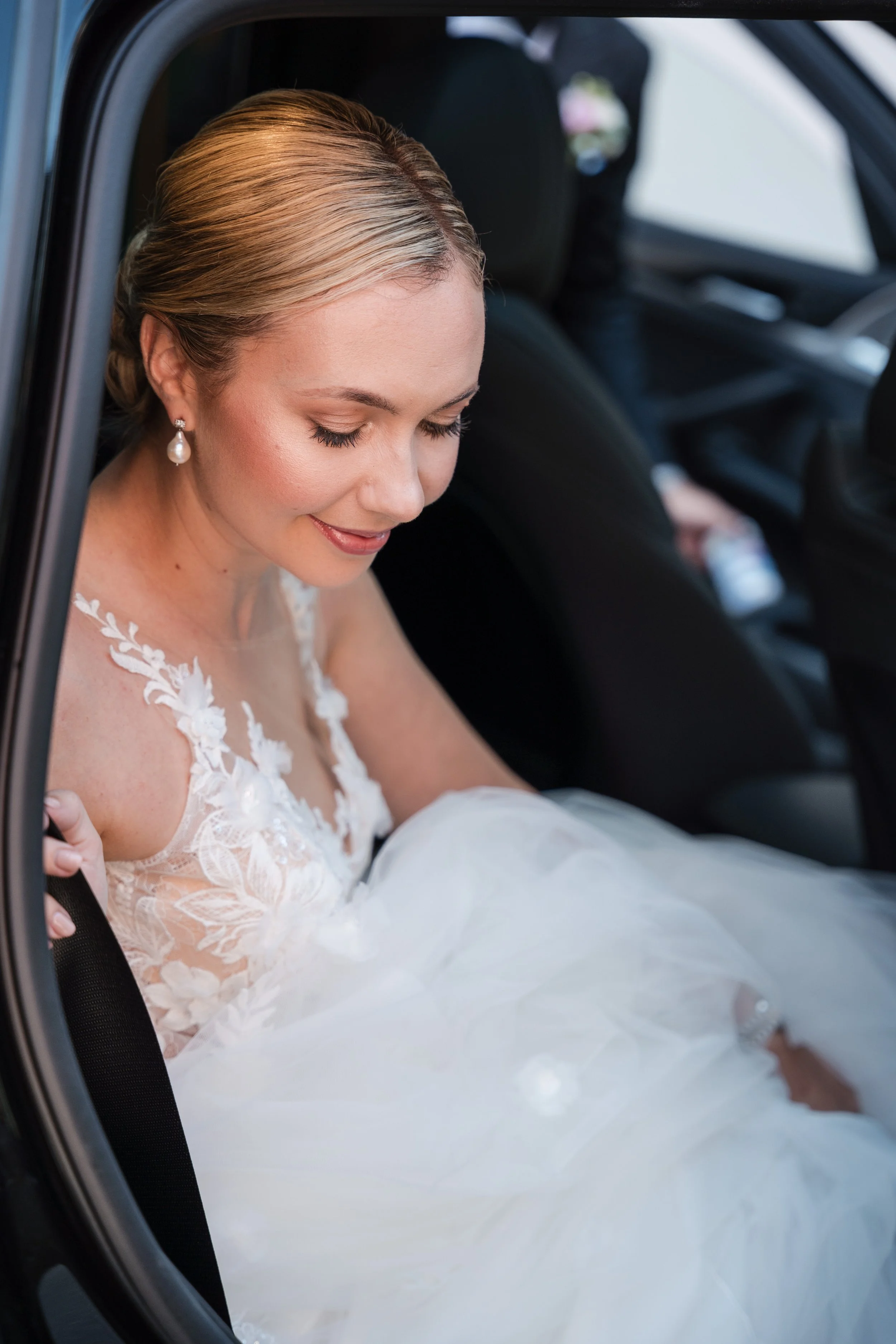Braut in Hochzeitskleid sitzt im Auto, lächelnd, mit geschlossener Augen, und sich auf den Sitz lehnend.