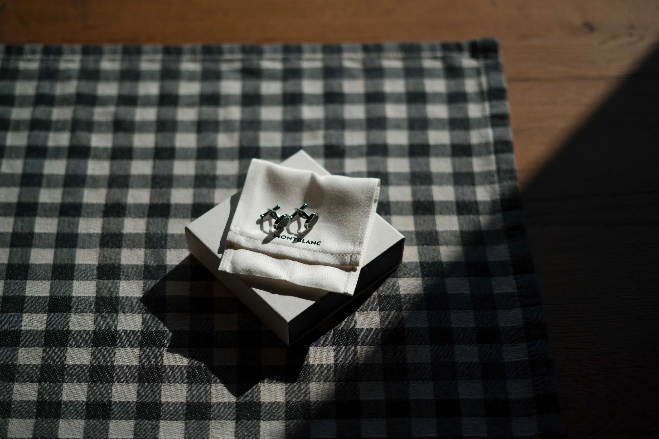 Silberne Manschettenknöpfe auf weißem Tuch auf einem schwarzen und weißen karierten Tischtuch.