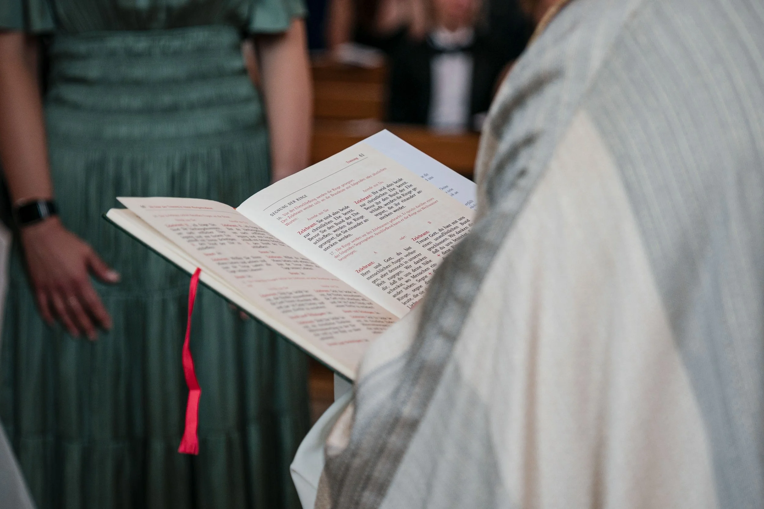 Person liest eine offene Bibel in einer Kirche oder Kapelle, im Hintergrund weitere Menschen, vermutlich bei einer religiösen Zeremonie.